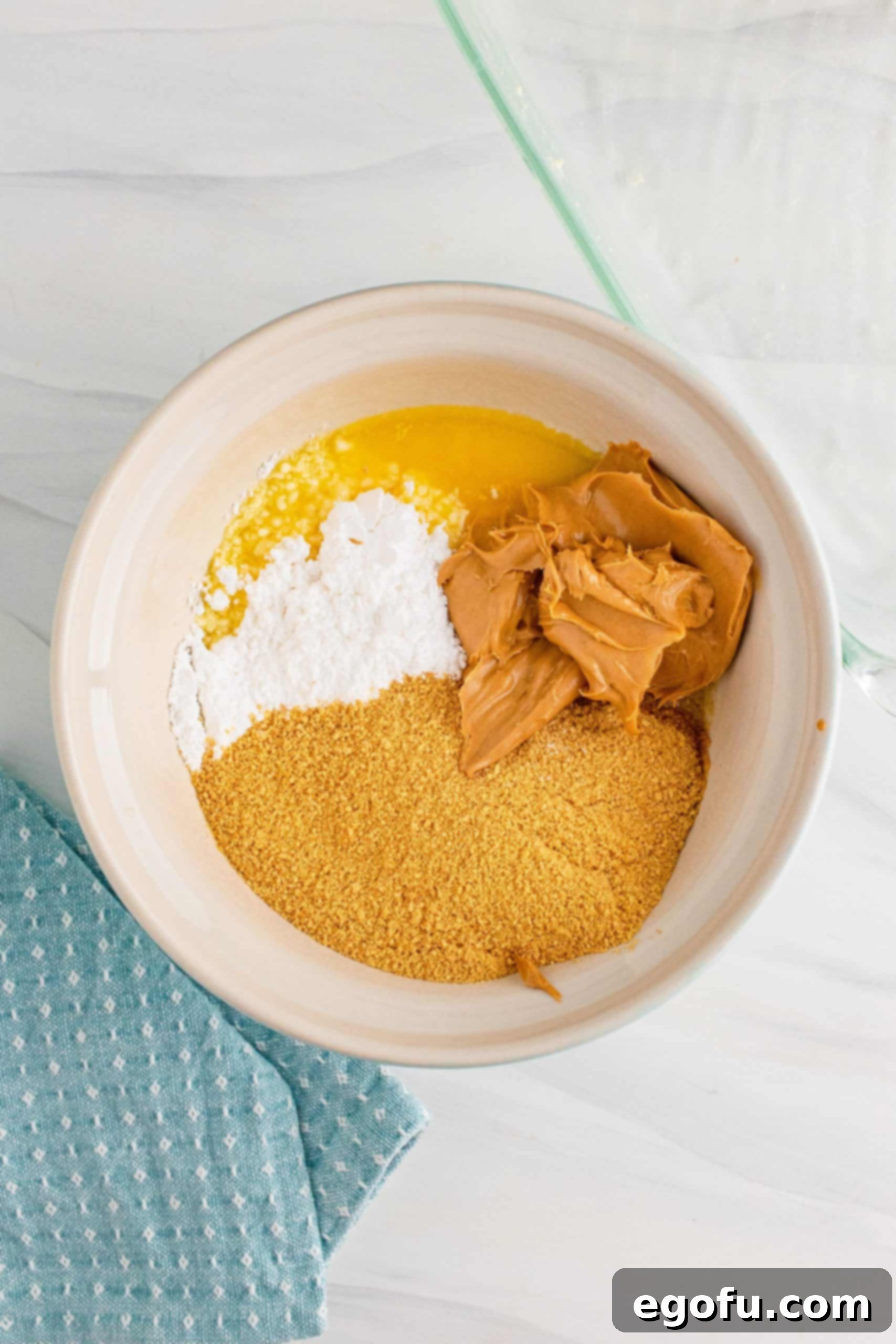 Grandma's No-Bake Peanut Butter Dream Bars 7 A close-up shot of graham cracker crumbs, creamy peanut butter, and powdered sugar being added to melted butter in a bowl.