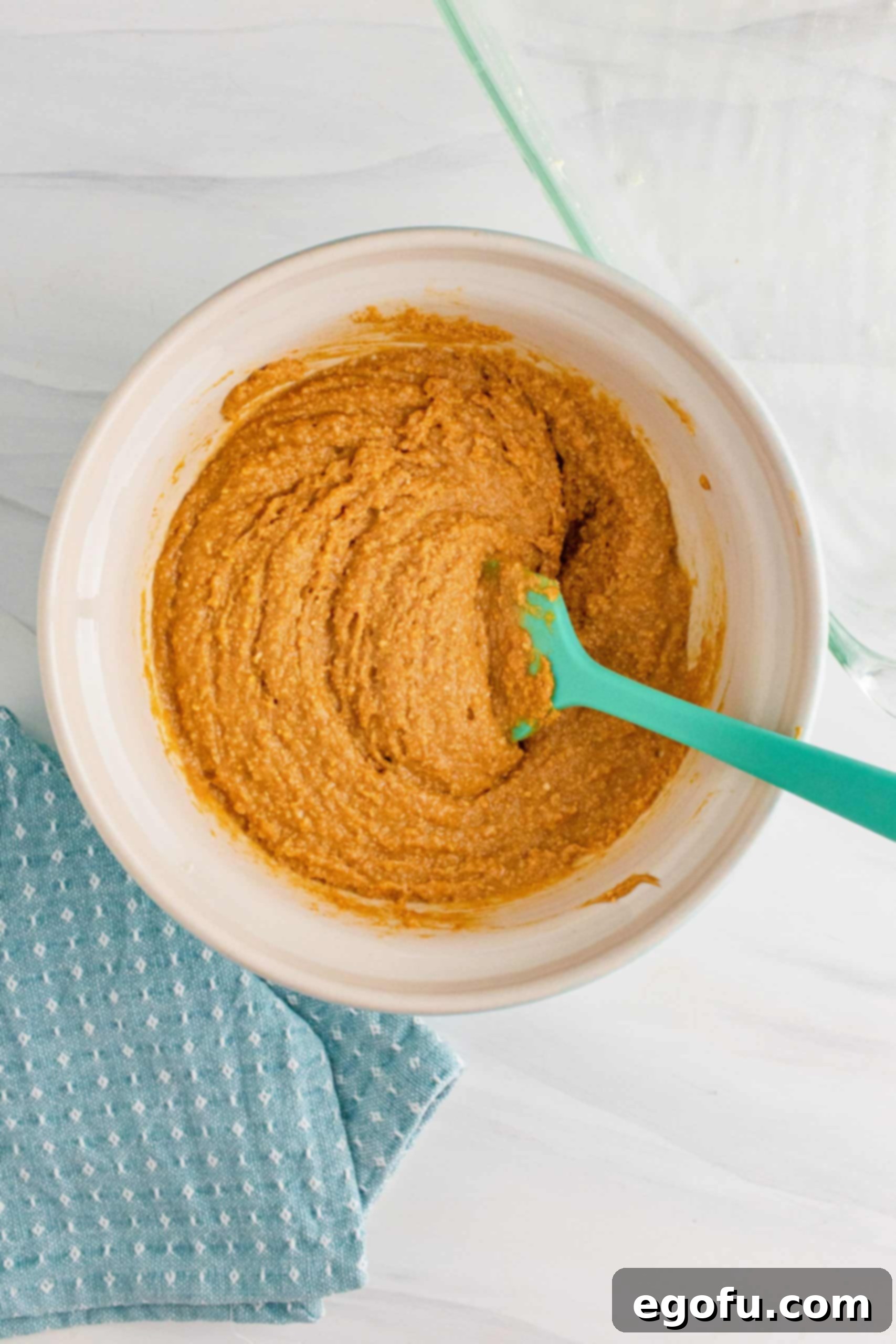 Grandma's No-Bake Peanut Butter Dream Bars 8 Peanut butter mixture being stirred in a bowl with an aqua-colored spatula, showing its creamy, combined texture.