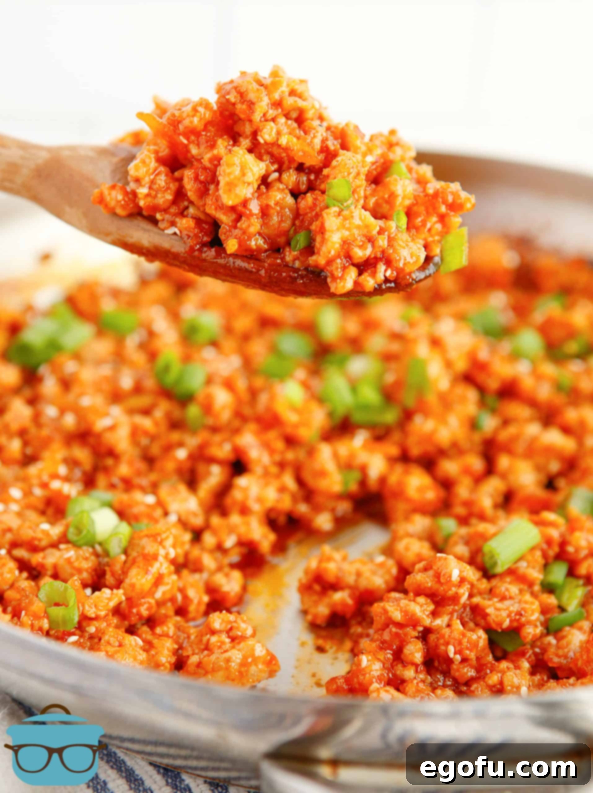 Skillet Orange Chicken Crumble 2 Close-up of savory Ground Orange Chicken served on a rustic wooden spoon, garnished with fresh green onions and sesame seeds, highlighting its rich, glossy glaze.