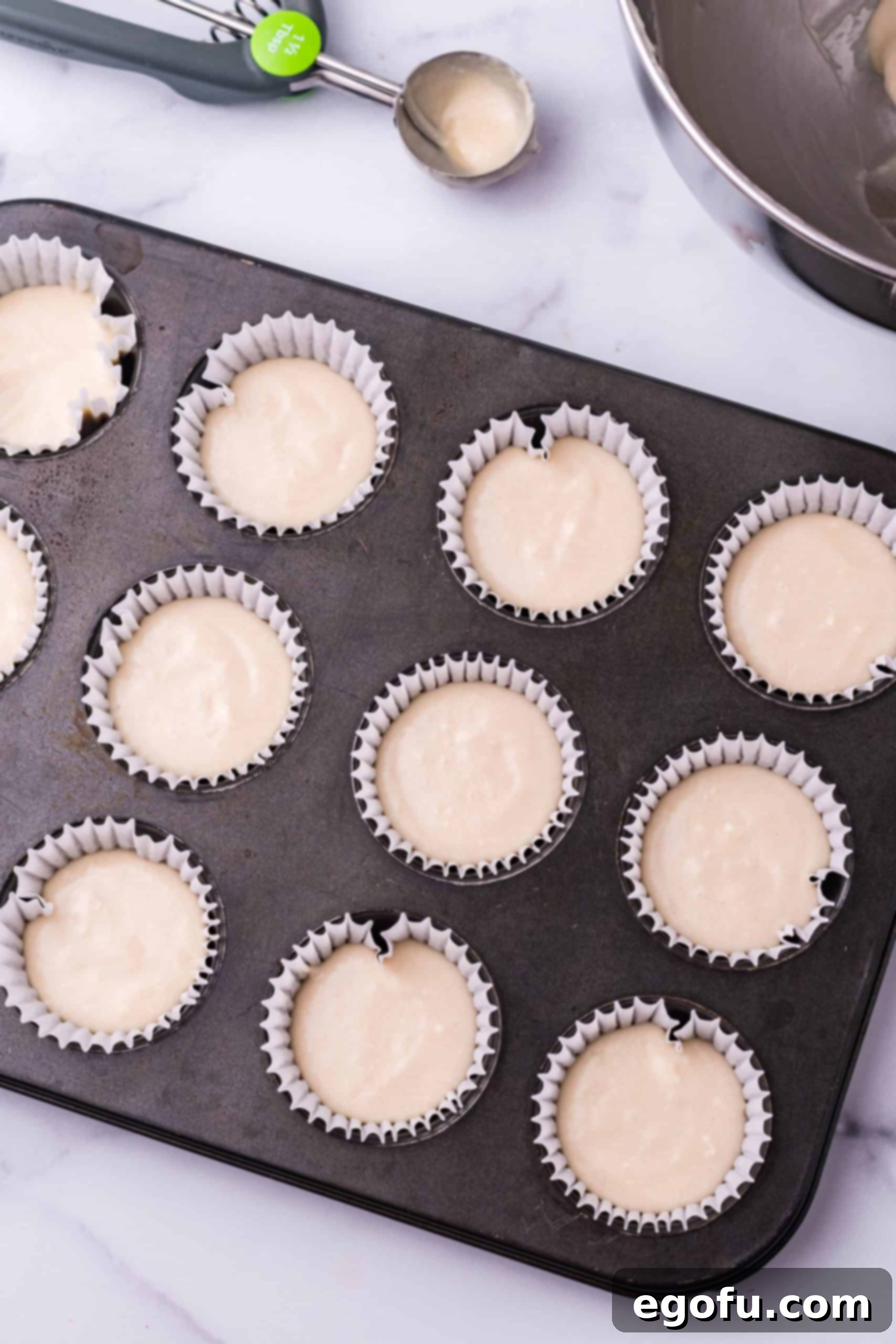 Freshly mixed cupcake batter neatly divided into cupcake liners within a baking pan, ready for the oven.