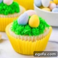 Close up of one decorated cupcake square image, showcasing vibrant green frosting and mini chocolate eggs.