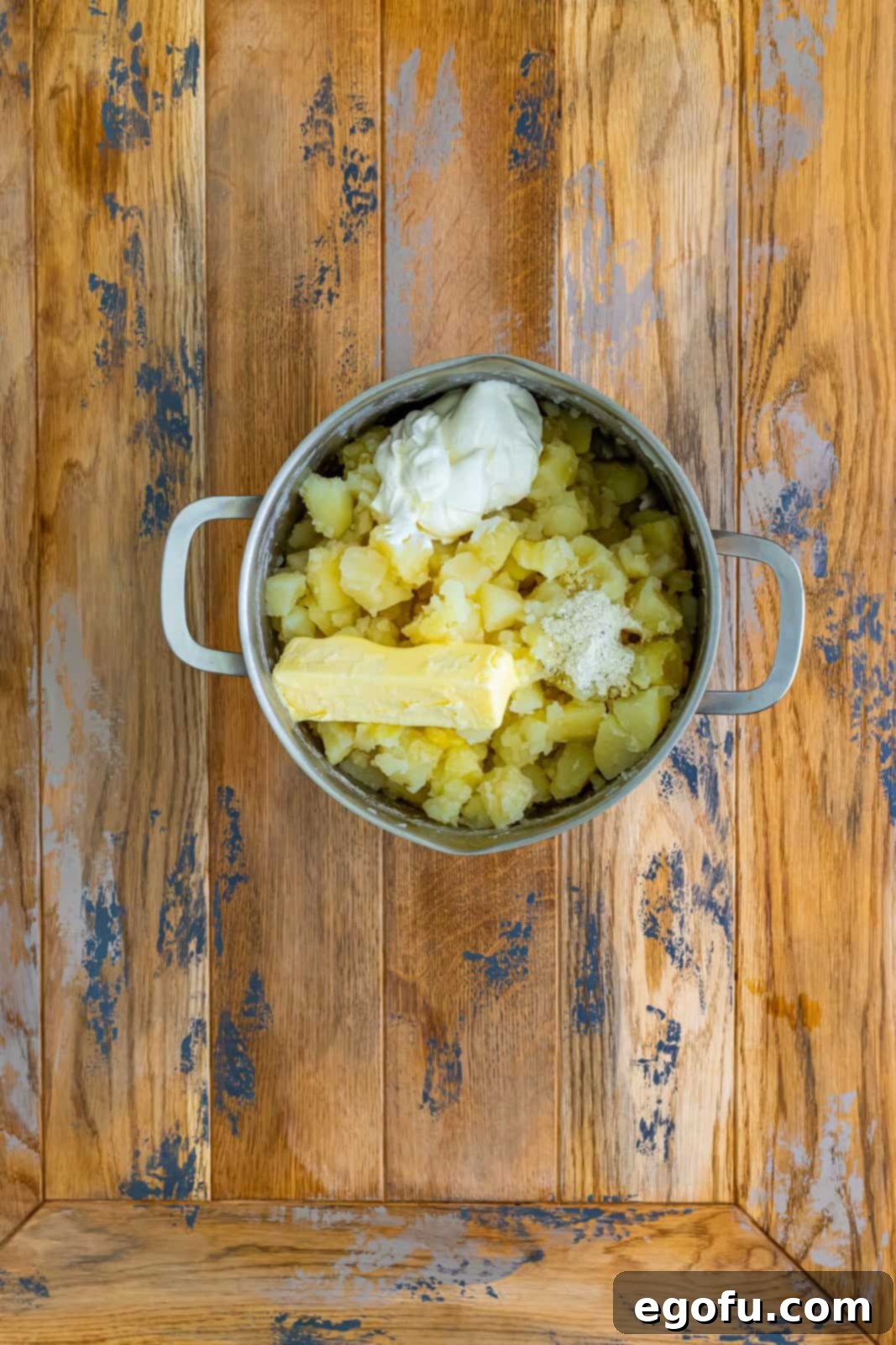 Cooked potatoes in a large pot, with cubes of butter, a dollop of sour cream, and ranch seasoning, ready to be mashed into a luxurious, creamy topping.