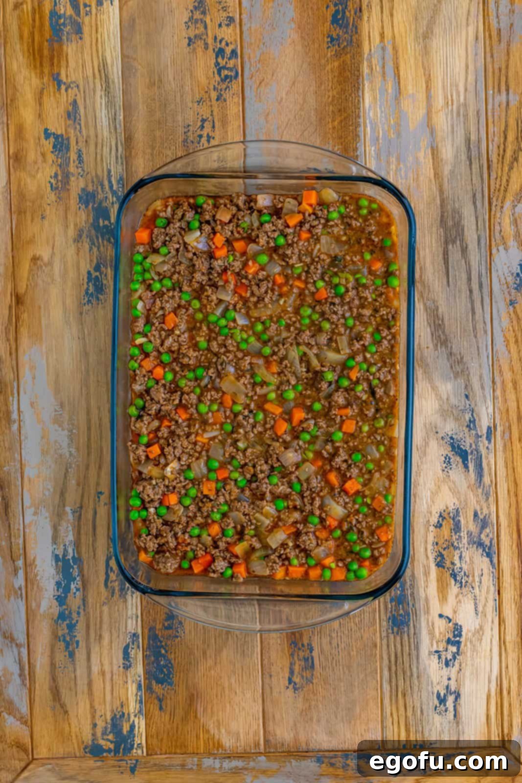 The savory meat and vegetable mixture evenly spread in a clear glass baking dish, forming the delicious and hearty base of the Shepherd's Pie.