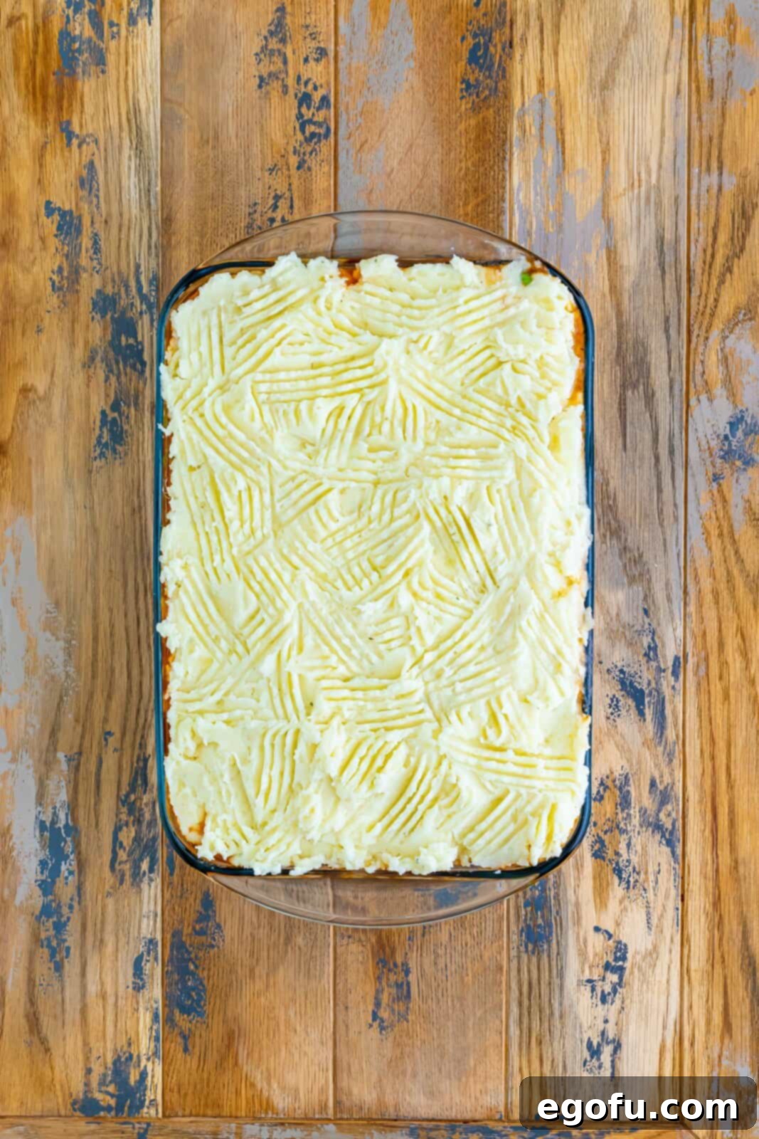 Smooth, creamy mashed potatoes carefully and evenly spread over the rich ground beef mixture in a baking dish, creating a perfect topping ready for the oven.
