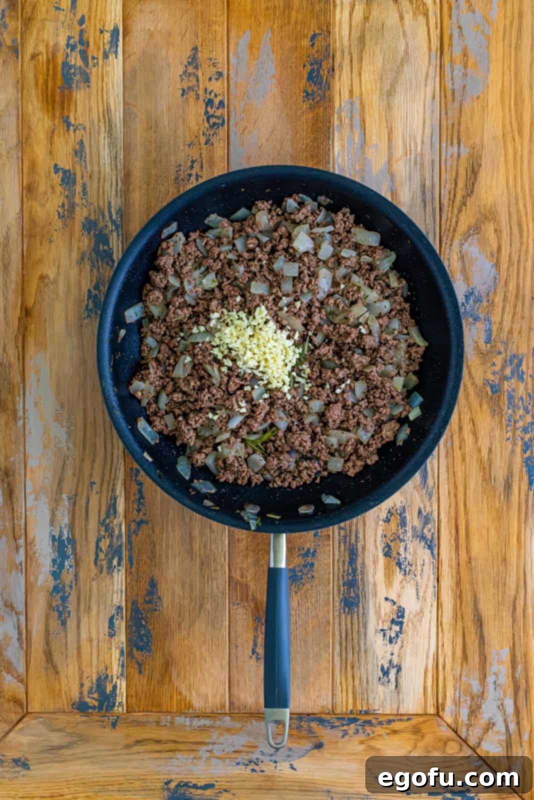 Freshly minced garlic being expertly stirred into the perfectly cooked ground beef and onion mixture in the skillet, releasing its pungent aroma and enhancing the savory depth.