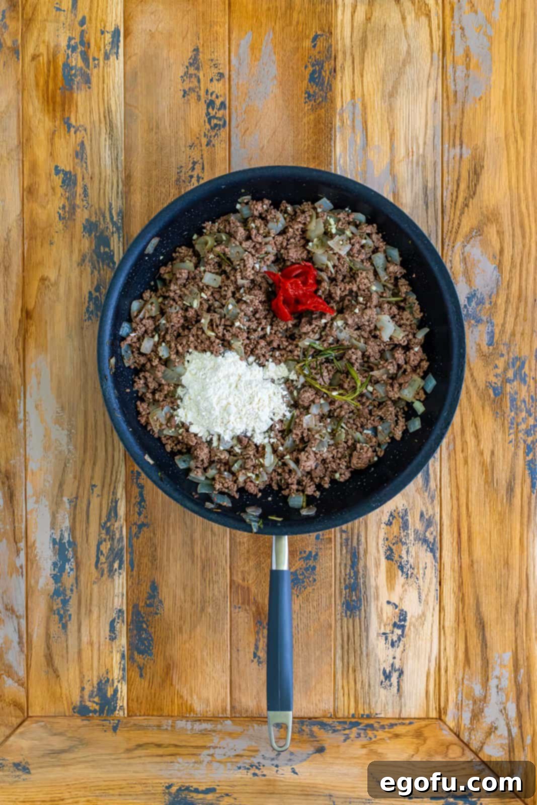 All-purpose flour and rich tomato paste added to the ground beef mixture in a skillet, skillfully stirred to form the beginnings of a thick, savory gravy.
