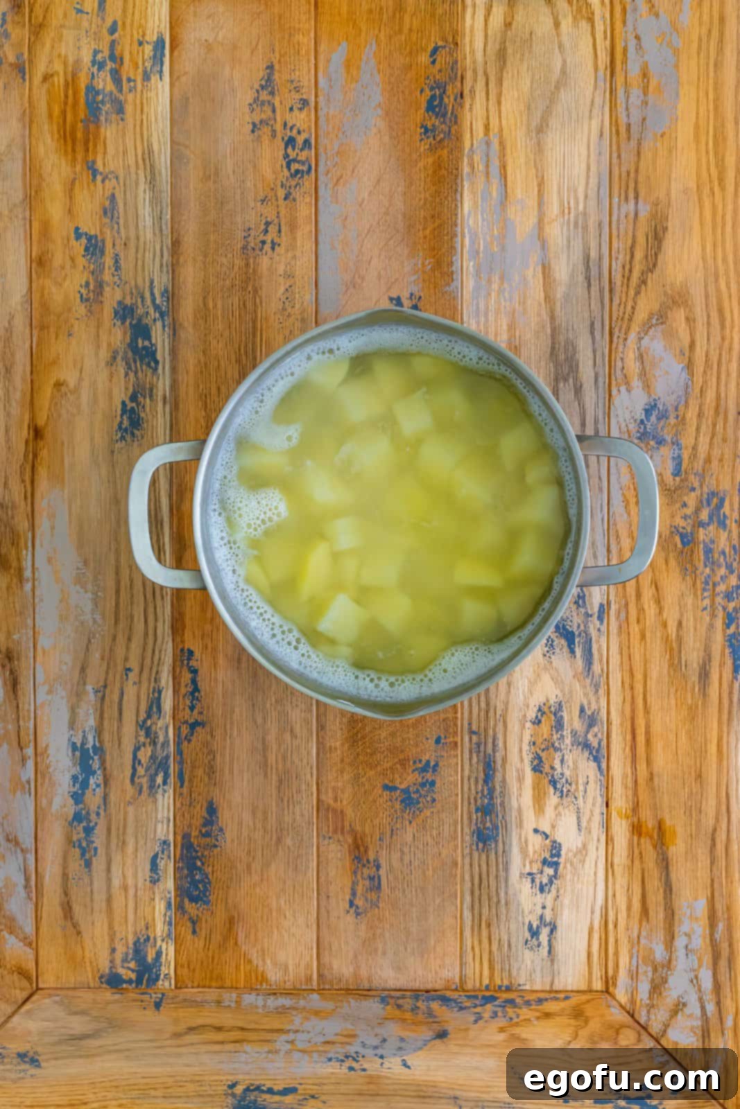 Diced potatoes boiling vigorously in hot water in a large pot on the stovetop, softening beautifully to create the creamy mashed topping for the pie.