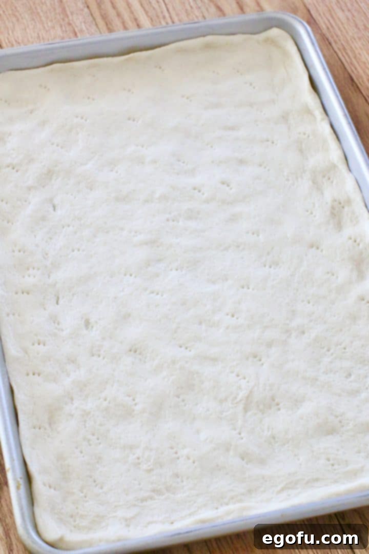 pizza crust spread out onto a rectangle baking sheet