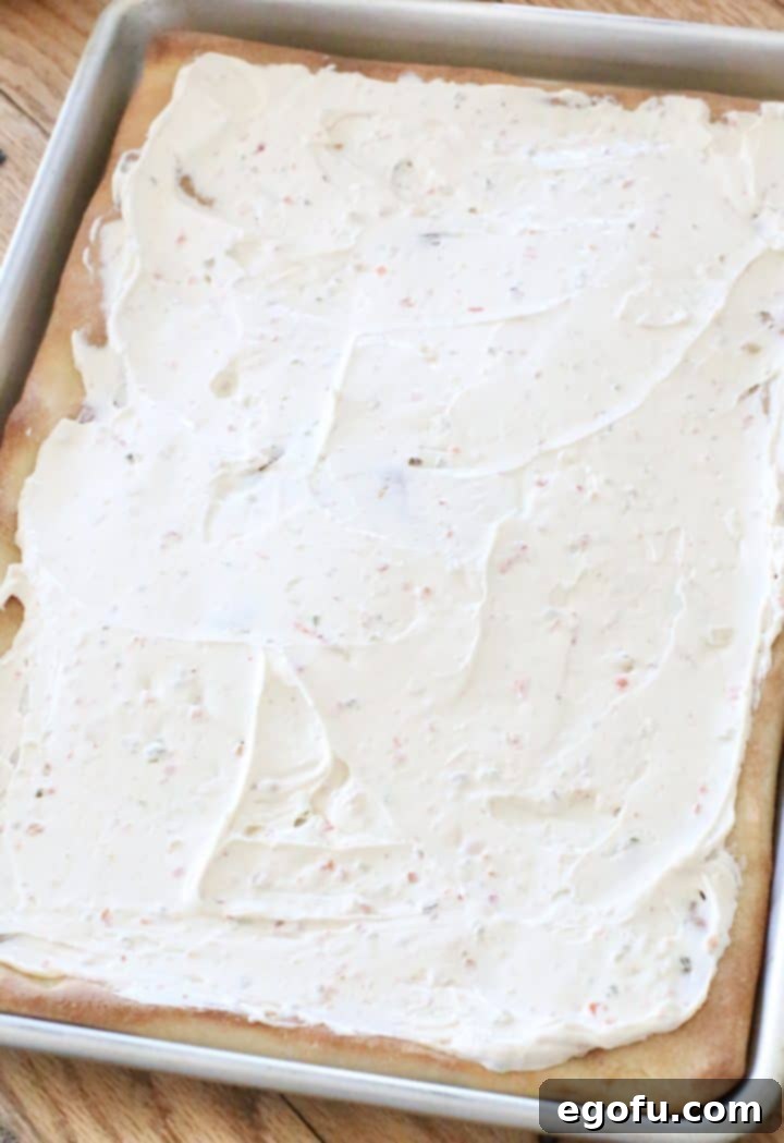 vegetable cream cheese spread evenly over a baked pizza crust in a baking pan