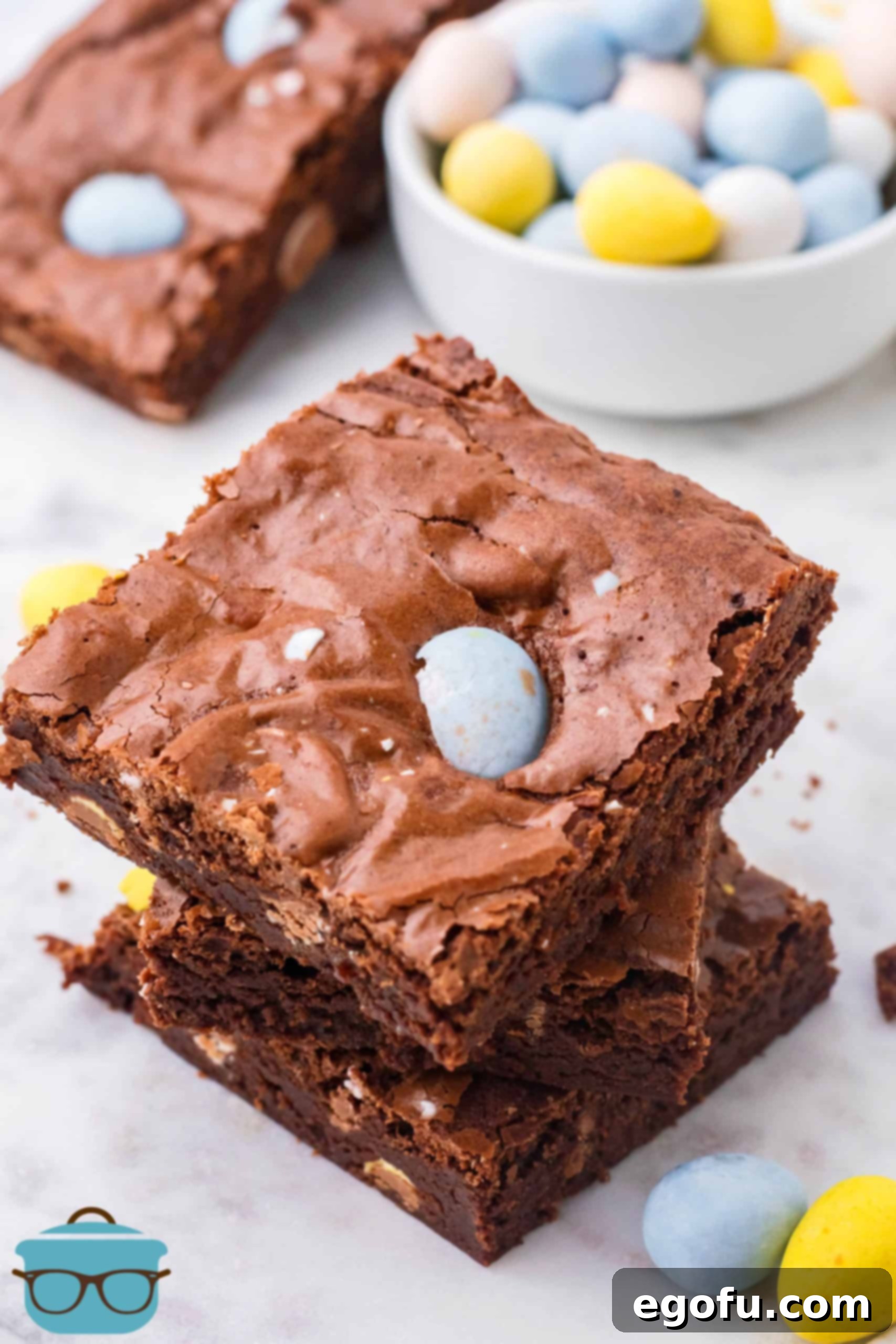 Fudgy Easter Egg Brownie Delights 2 Three stacked Easter Egg Brownies on a marble surface, showcasing their fudgy texture and colorful Cadbury eggs peeking through.