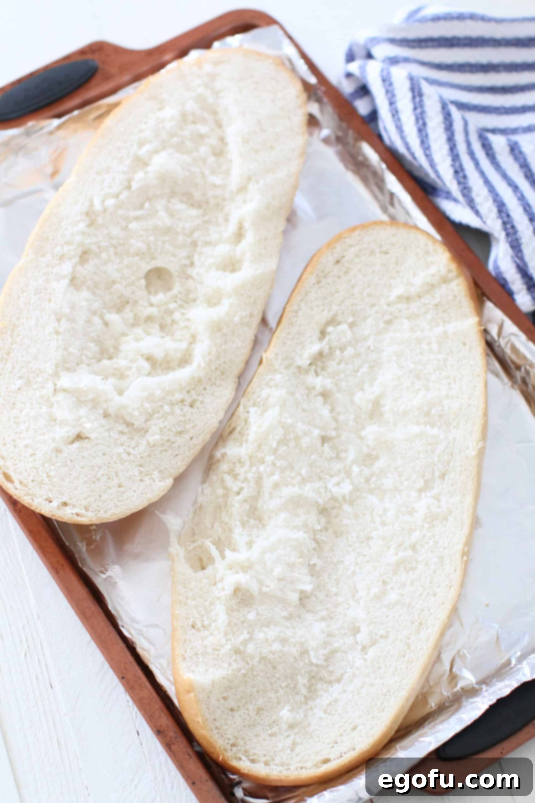 two halves of sliced Italian bread on an an aluminum foil covered baking sheet.