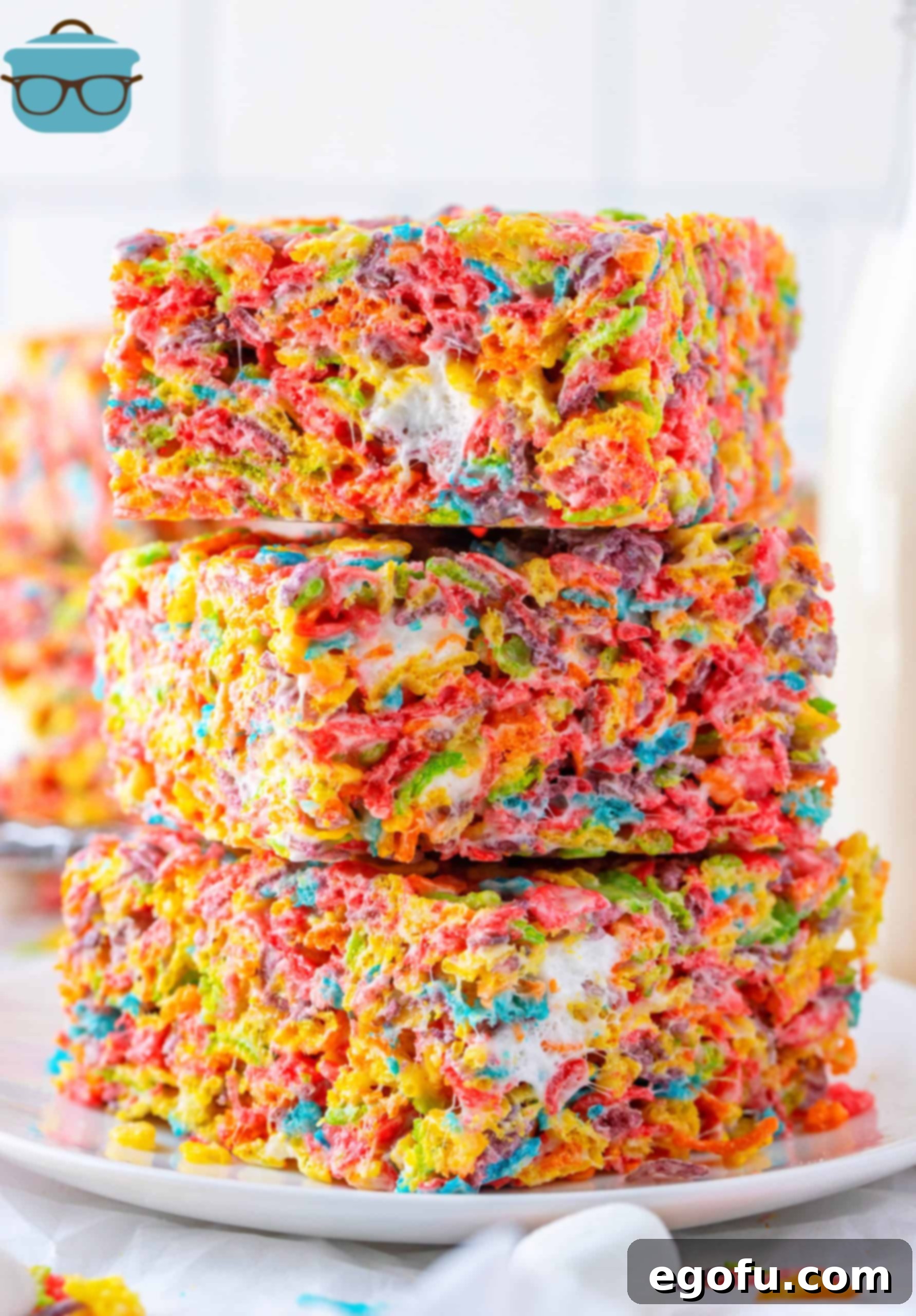 Three stacked Fruity Pebbles Treats on a white plate, showcasing their vibrant colors and gooey texture.