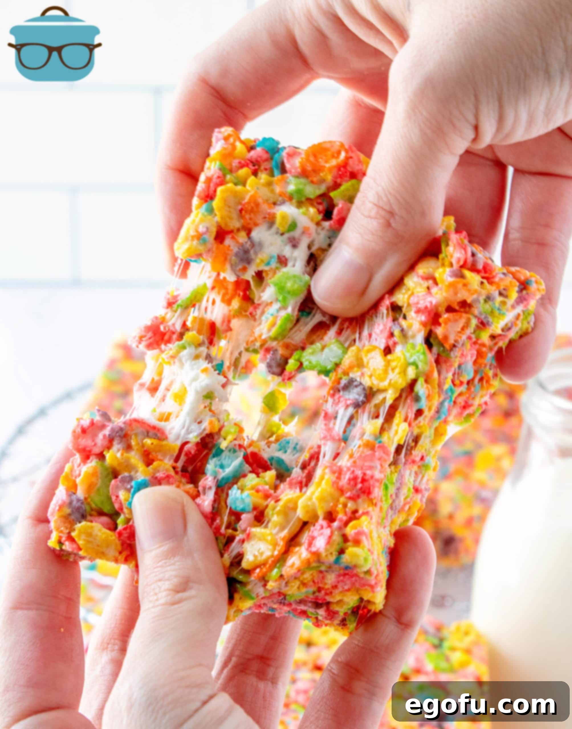 A hand pulling apart one Fruity Pebbles Treat, showing its gooey, stretchy texture.
