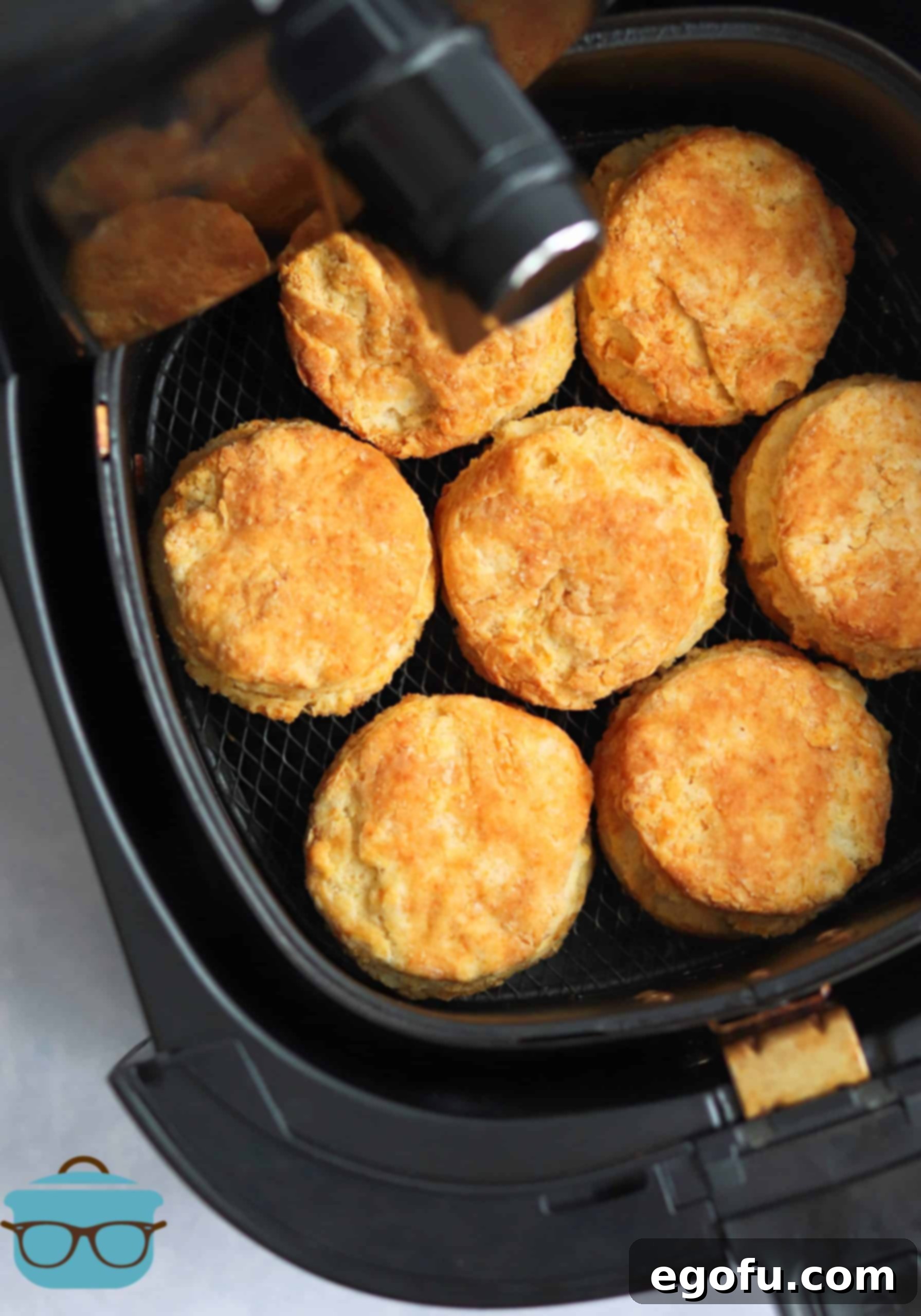 Perfectly air-fried golden brown buttermilk biscuits sitting in the air fryer basket, showcasing their fluffy texture and readiness to be served.