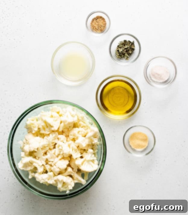 Ingredients for Air Fryer Roasted Cauliflower, including cauliflower, olive oil, pink Himalayan salt, garlic powder, basil, lemon pepper seasoning, and fresh lemon juice, laid out on a surface.