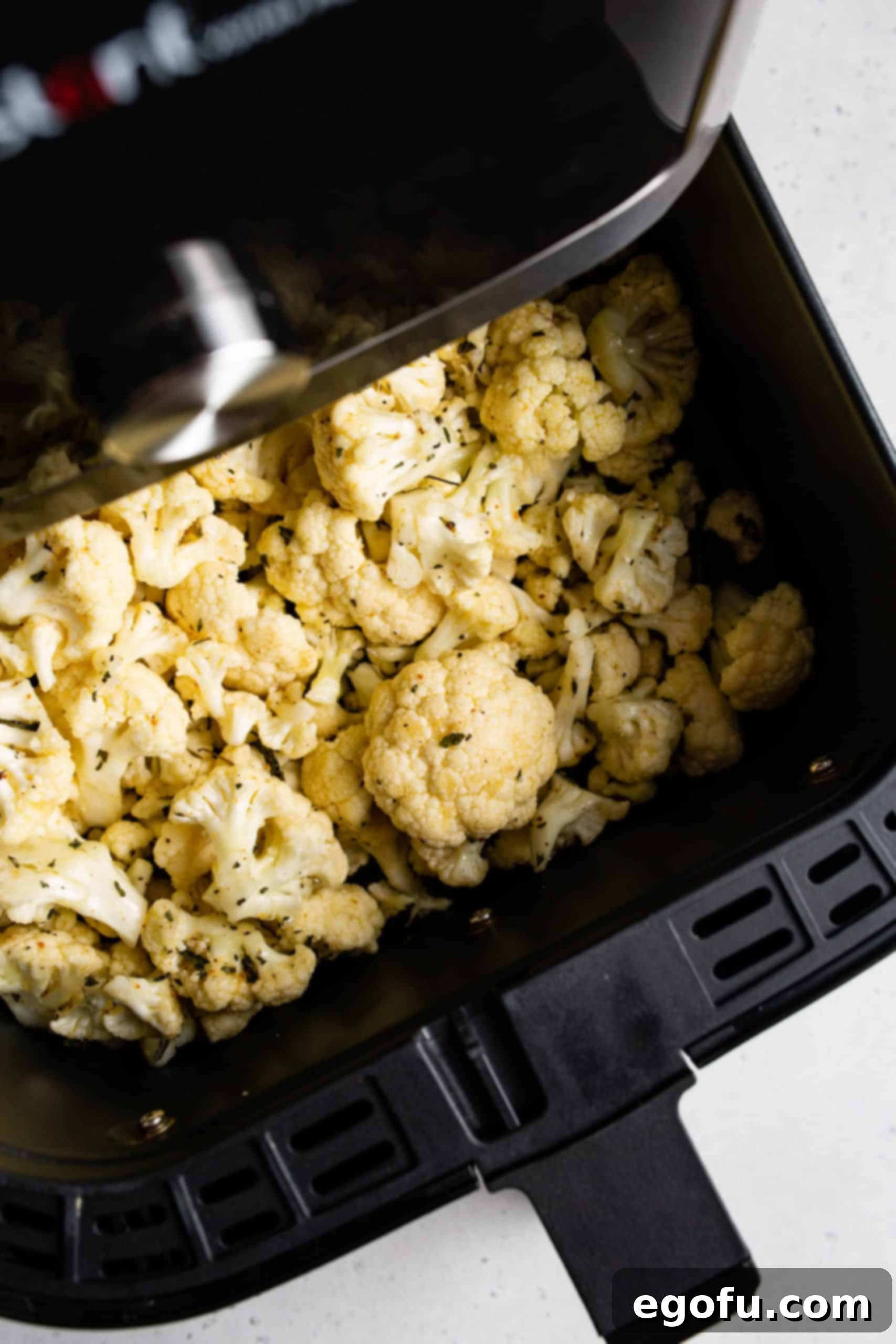 Seasoned cauliflower florets arranged inside an air fryer basket, ready for cooking.