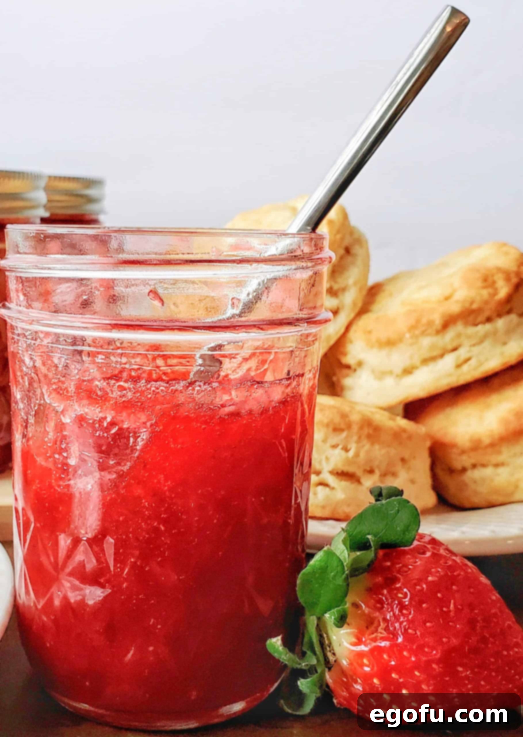 A single jar of Strawberry Rhubarb Jam, cooled and set, with a spoon resting in it, inviting a taste. The jar is placed on a light-colored surface.