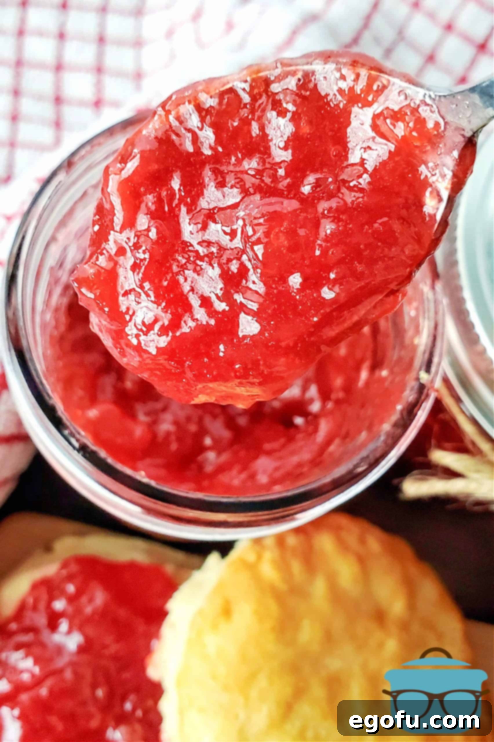 An overhead shot showing a spoon full of set Strawberry Rhubarb Jam held above an open jar, showcasing its rich color and inviting texture.