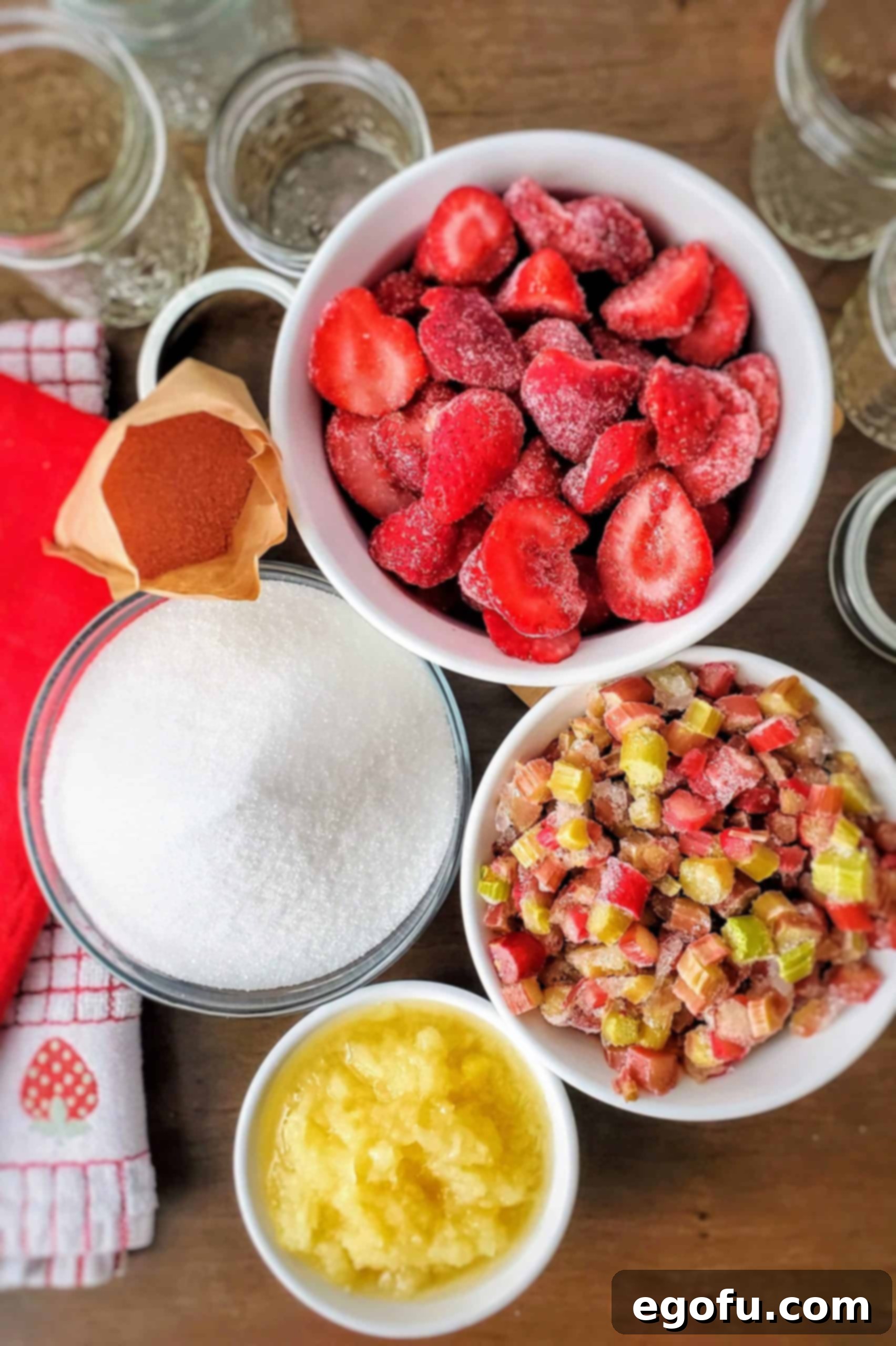 A vibrant flat lay image showcasing the essential ingredients for Strawberry Rhubarb Jam: frozen sliced unsweetened strawberries, frozen diced rhubarb, a can of crushed pineapple in 100% juice, granulated sugar, and a package of strawberry-flavored gelatin.