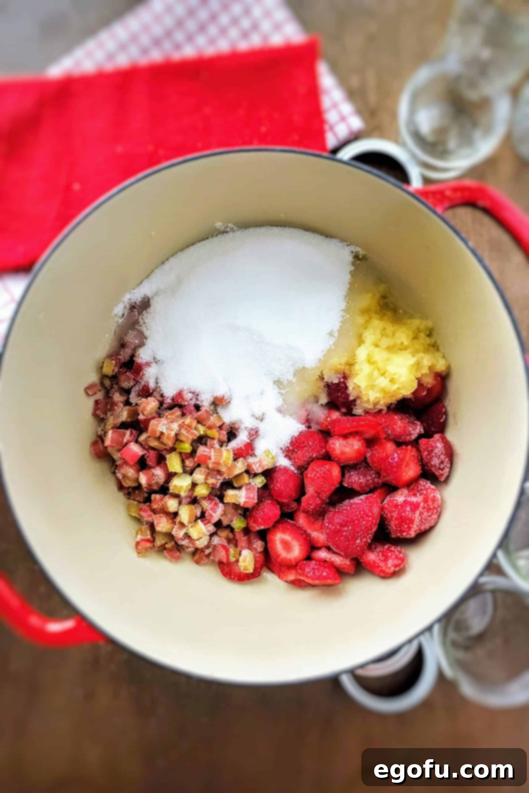 A large saucepan filled with the initial ingredients for strawberry rhubarb jam: frozen diced rhubarb, frozen sliced strawberries, crushed pineapple (undrained), and granulated sugar, ready to be heated.