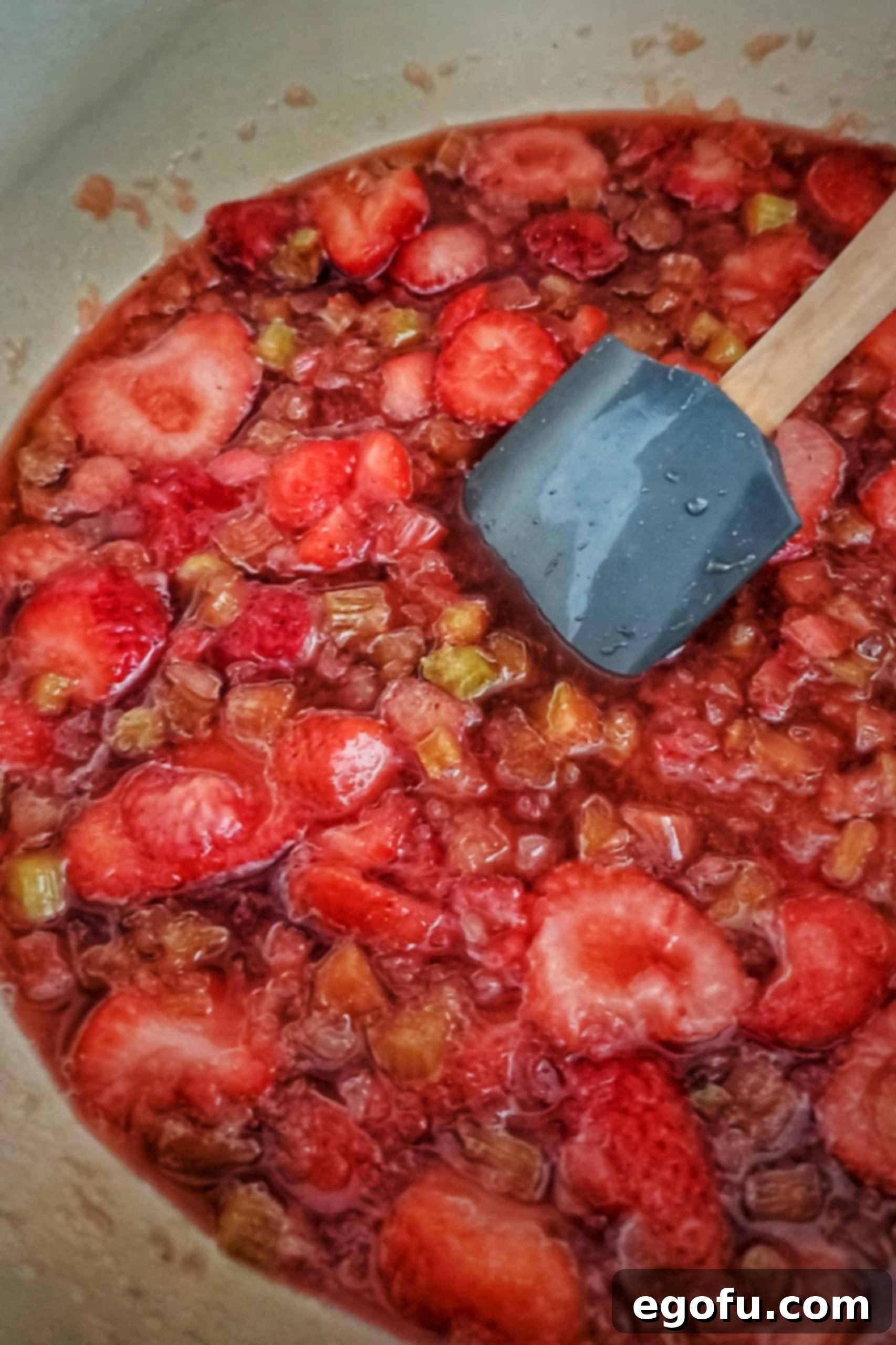 Close-up shot of the fruit mixture boiling vigorously in a saucepan over medium-high heat, being actively stirred to break down the fruit pieces.