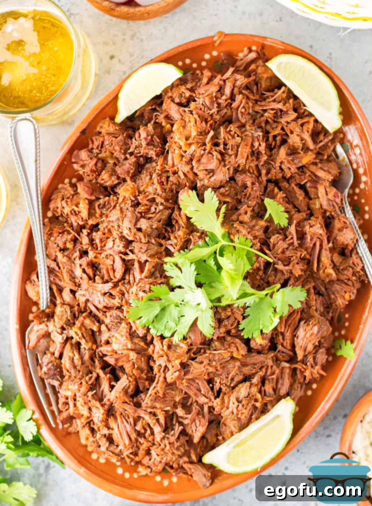 Overhead view of Instant Pot Barbacoa on a platter, garnished with cilantro and lime wedges, emphasizing its presentation.