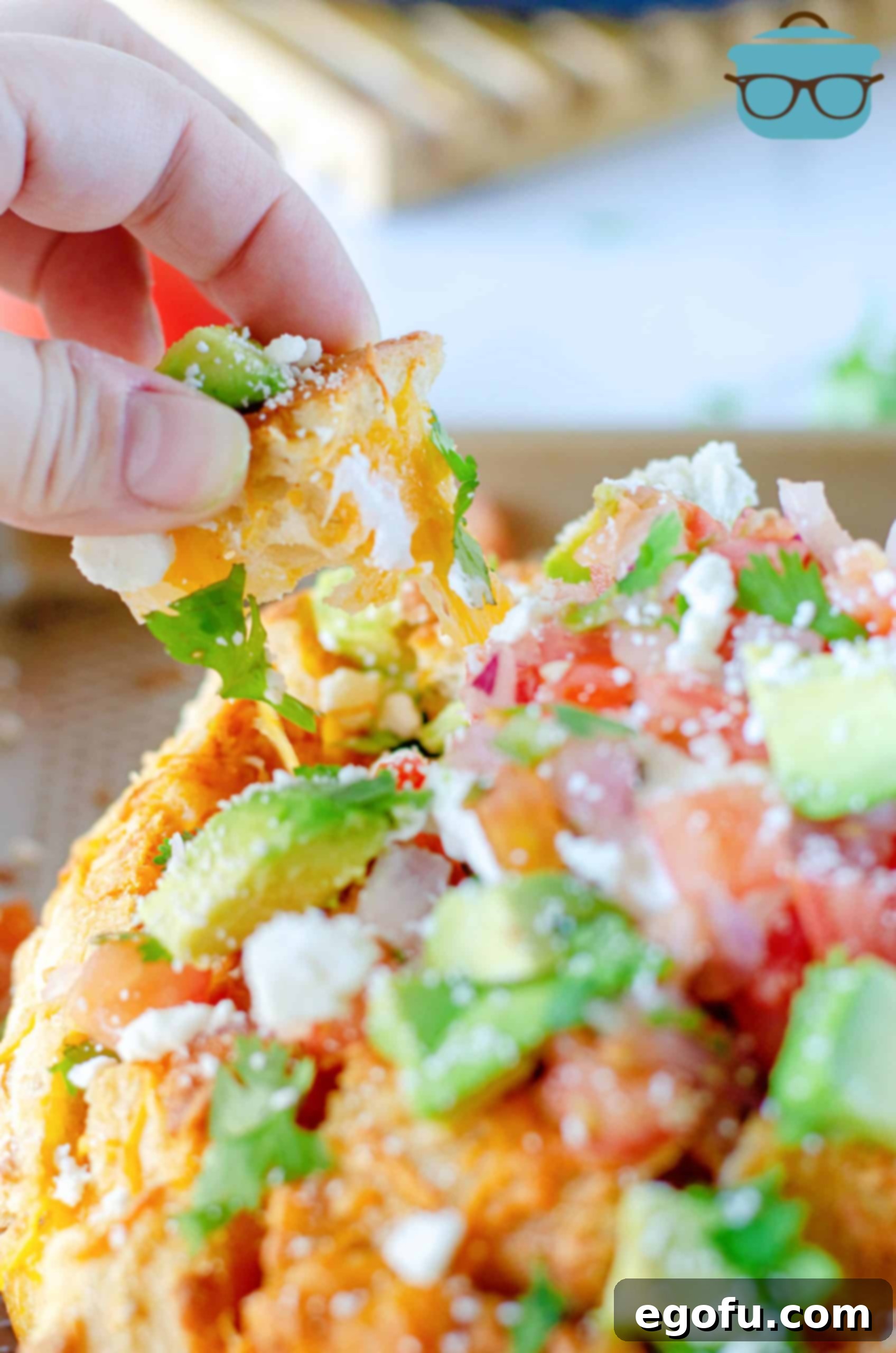 Hand pulling a piece out of Taco Pull Apart Bread, showcasing the melted cheese and vibrant toppings in a festive setting.