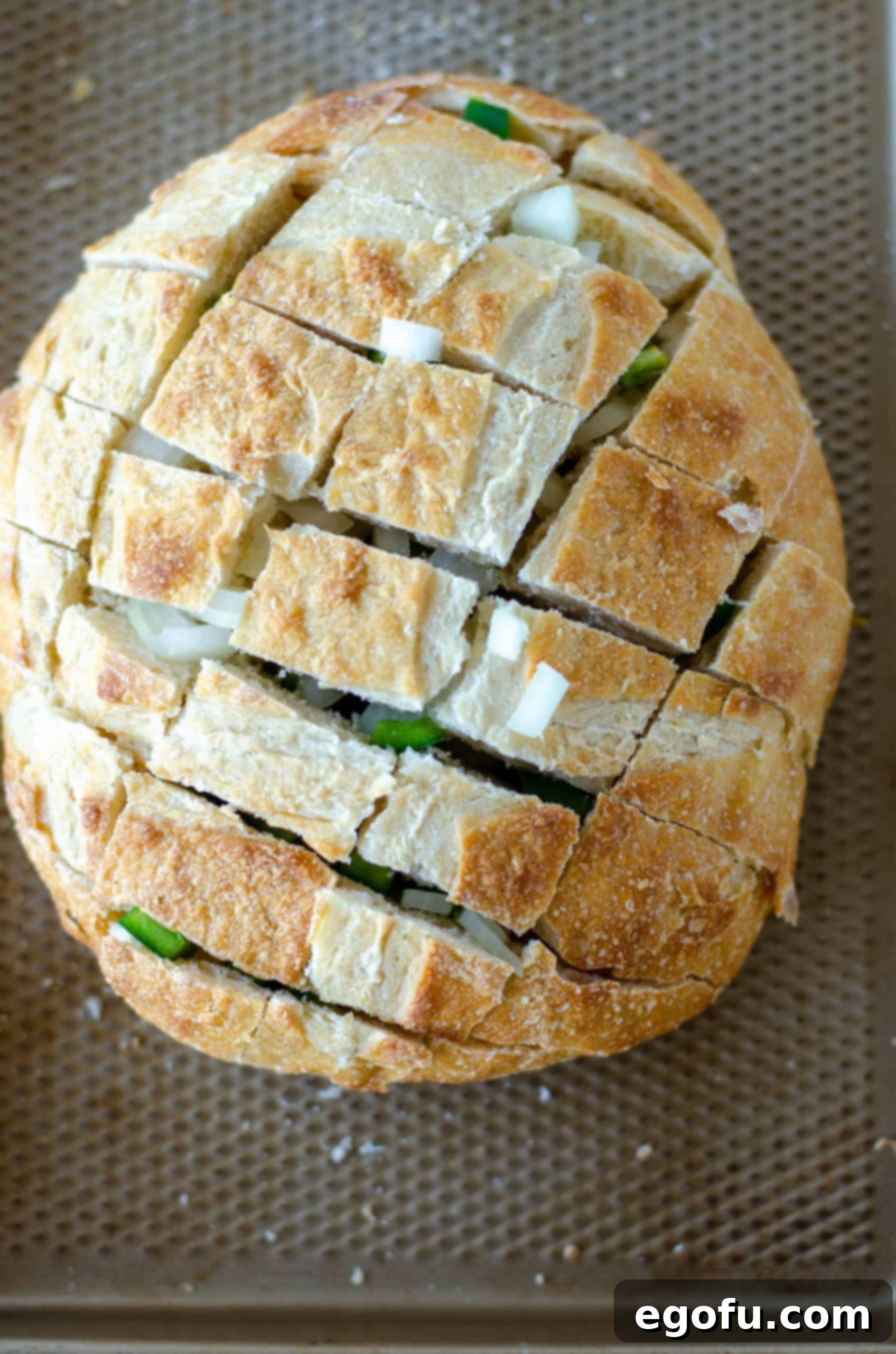 Diced onion and jalapeño carefully added into the crevices of the cut bread loaf on a baking sheet, ready for the next step.