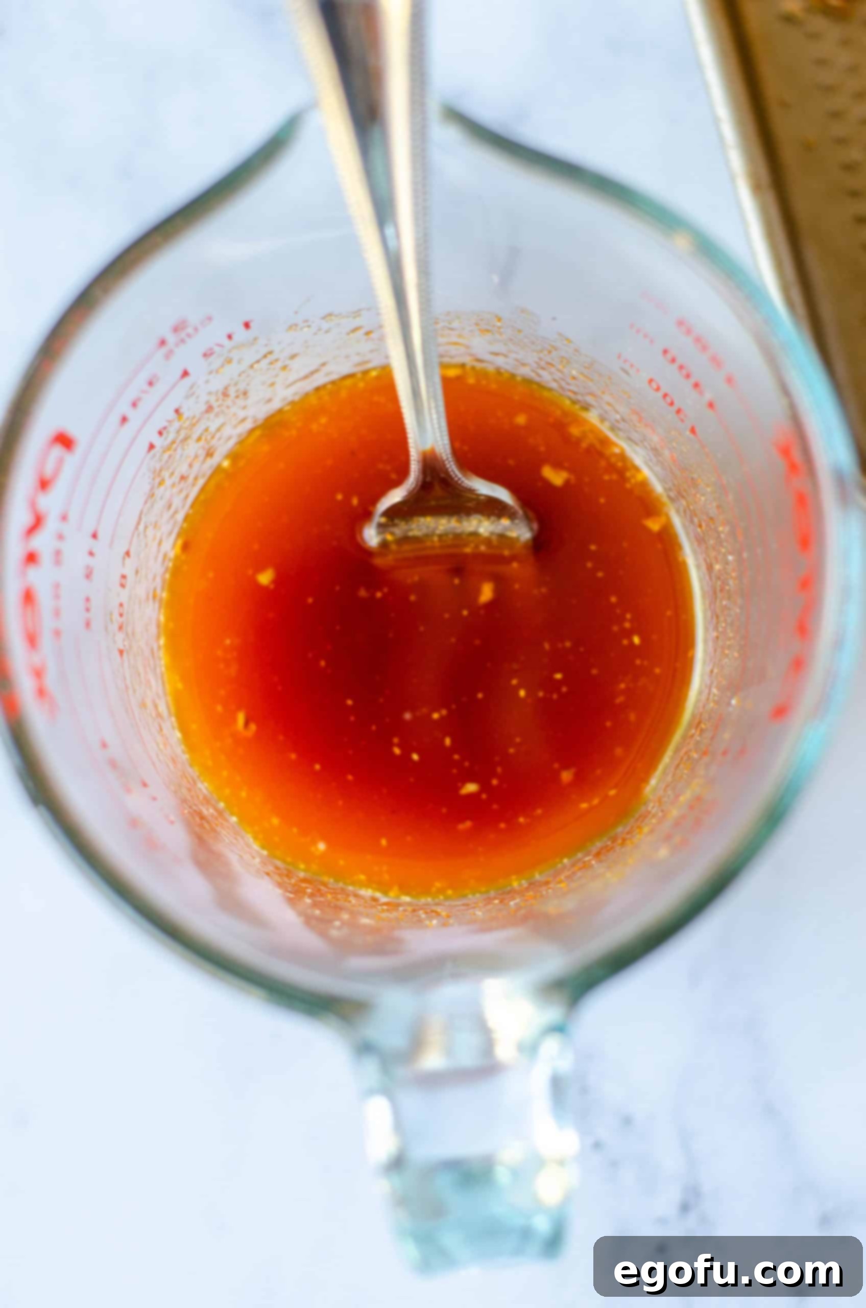 Melted butter and taco seasoning being stirred together in a measuring cup with a fork, creating a flavorful liquid mixture.