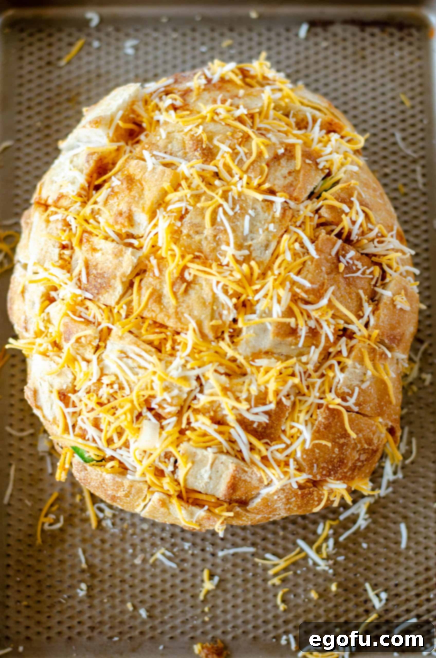 Shredded Colby Jack and mozzarella cheese generously sprinkled and stuffed over the bread loaf on a baking sheet, ready for the oven.