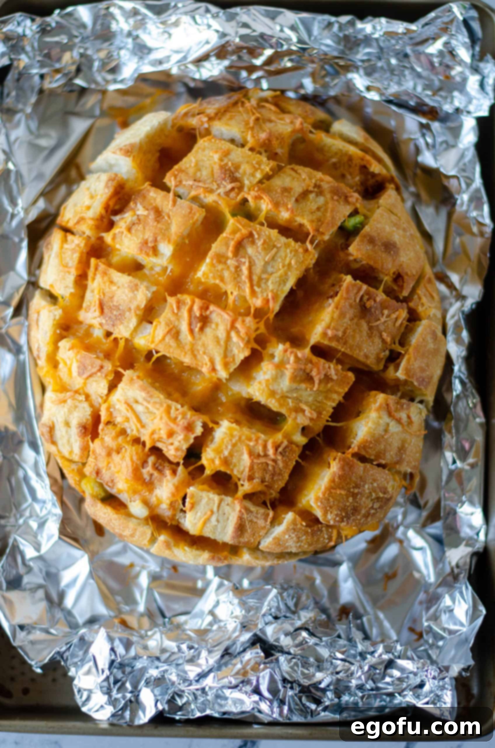 Finished Taco Pull Apart Bread in foil, showing bubbling melted cheese in the cut portions of the loaf, just removed from the oven.