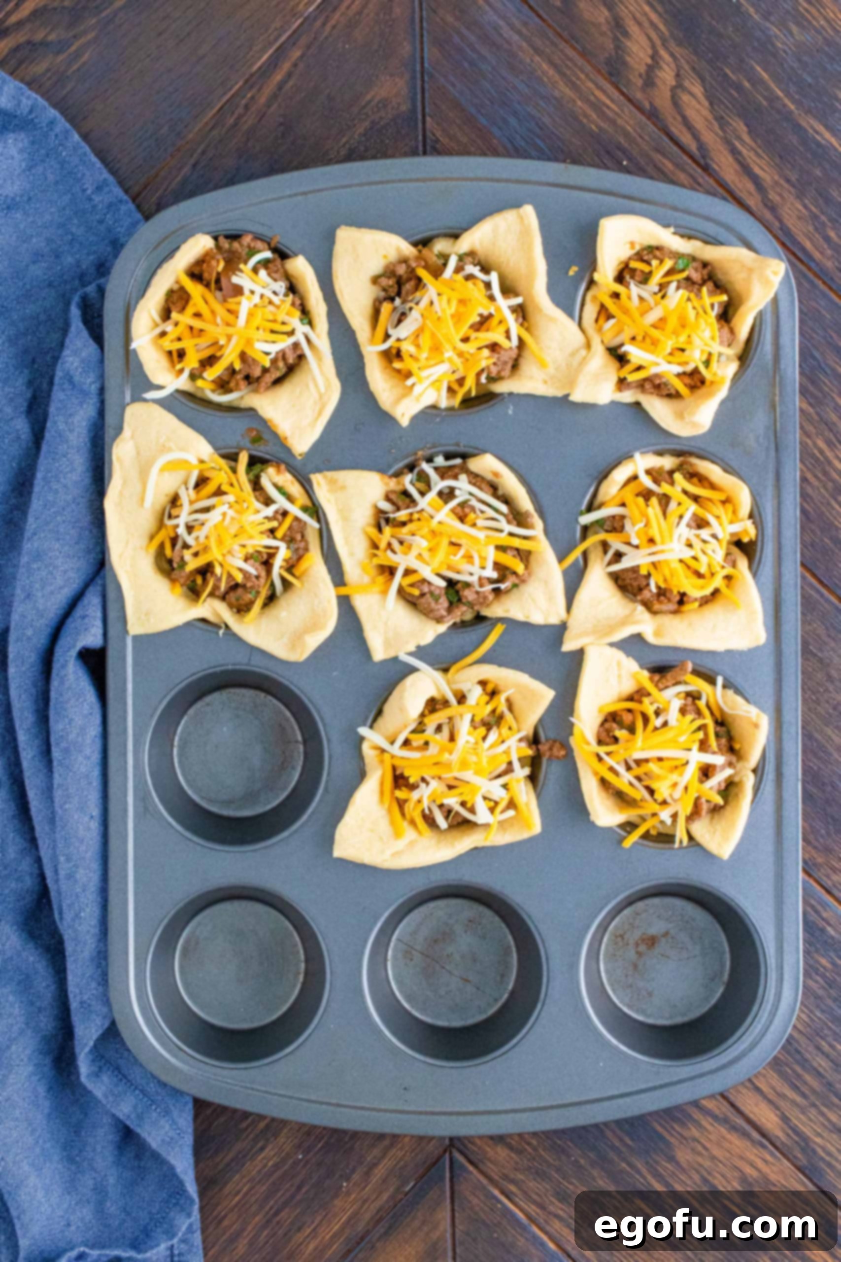 More cheese topping the taco meat in muffin tin, completing the filling layers.