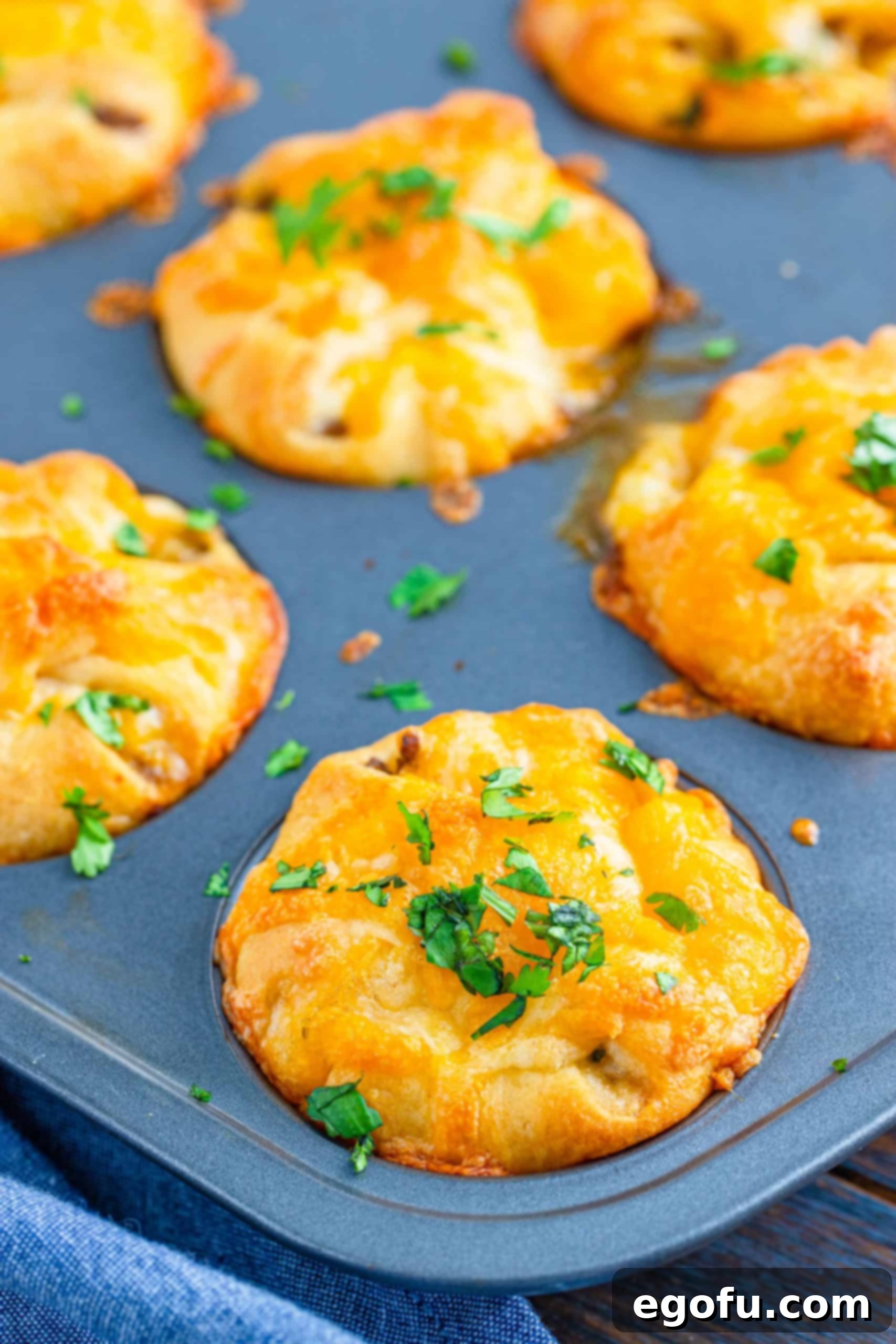 Finished Crescent Taco Cups in muffin tin with melted cheese and cilantro, hot out of the oven.