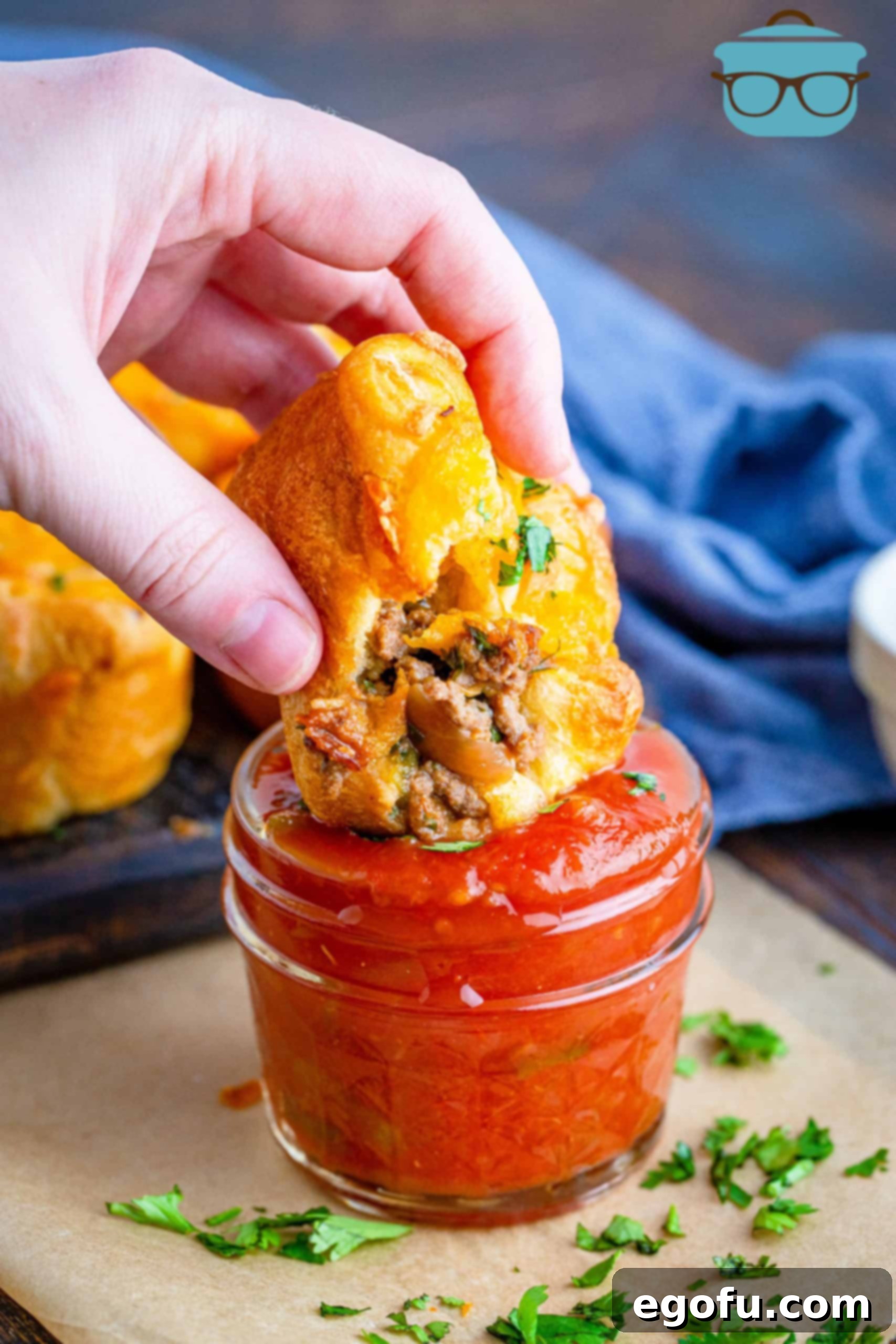 Hand dipping a golden Crescent Taco Cup in a jar of vibrant salsa, highlighting its appetizing appeal.
