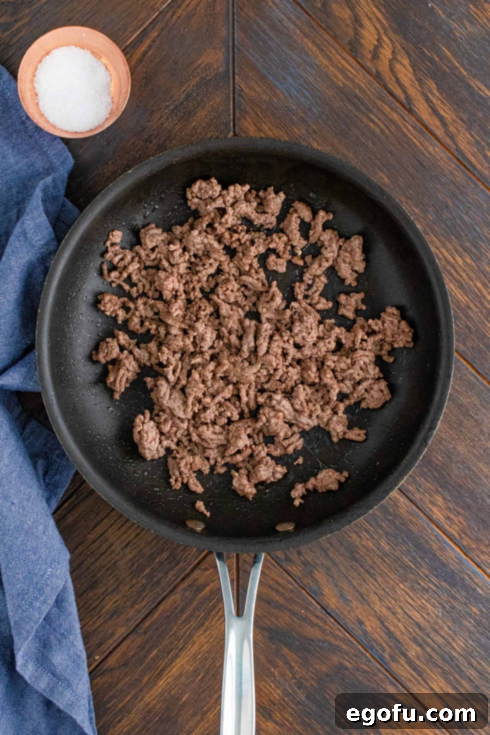 Cooked ground beef in pan with blue linen on the side of the pan, ready for seasoning.