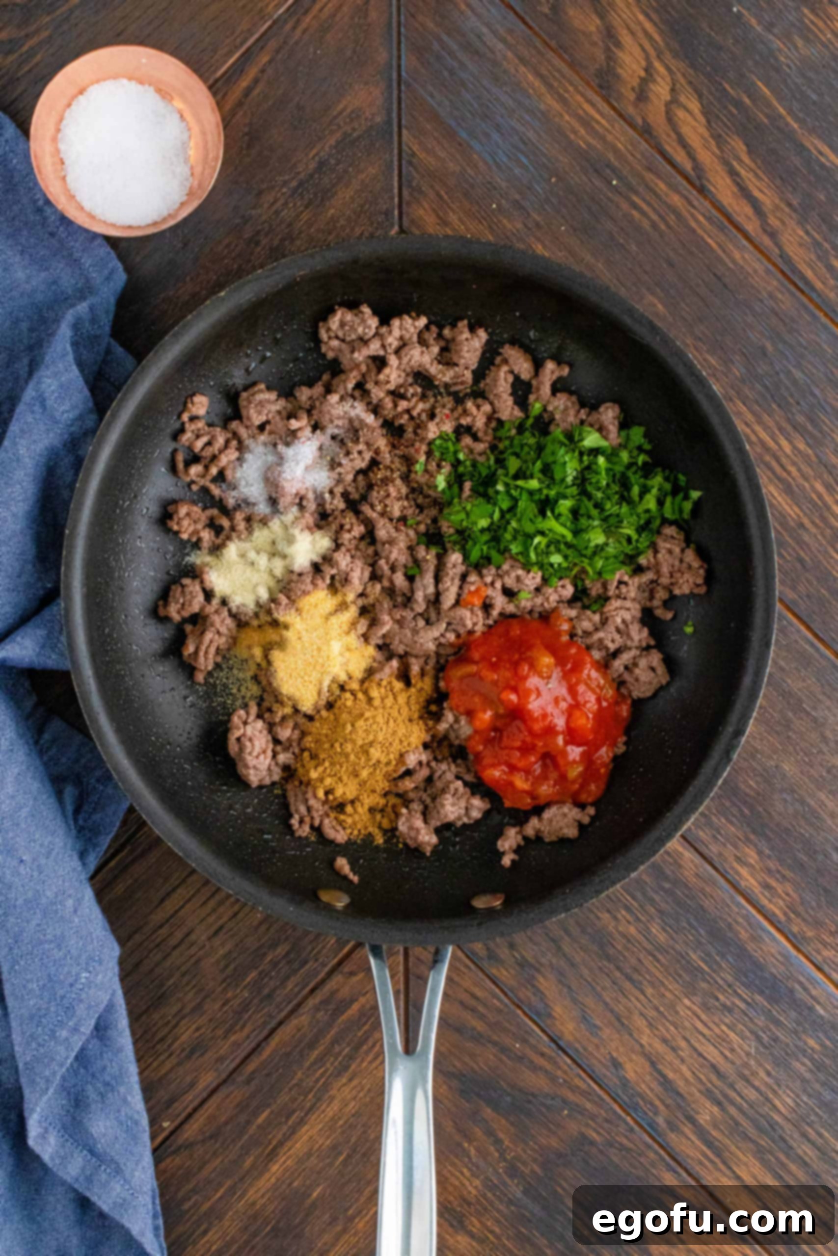 Cumin, garlic powder, onion powder, salt, pepper, salsa, water, and cilantro added to cooked ground beef in pan, creating the taco filling.
