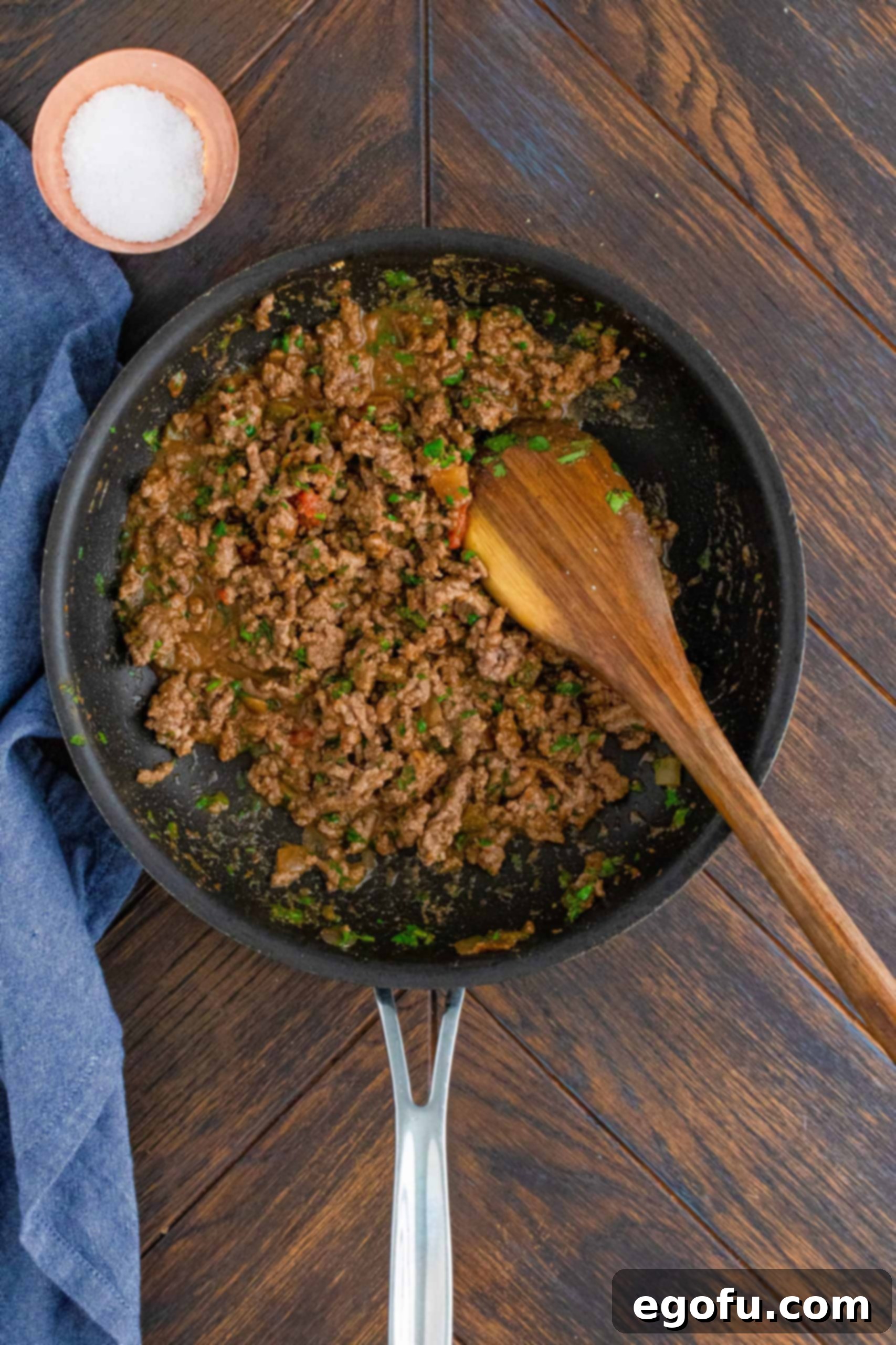 All taco ingredients stirred up in pan with a wooden spoon, simmering to combine flavors.
