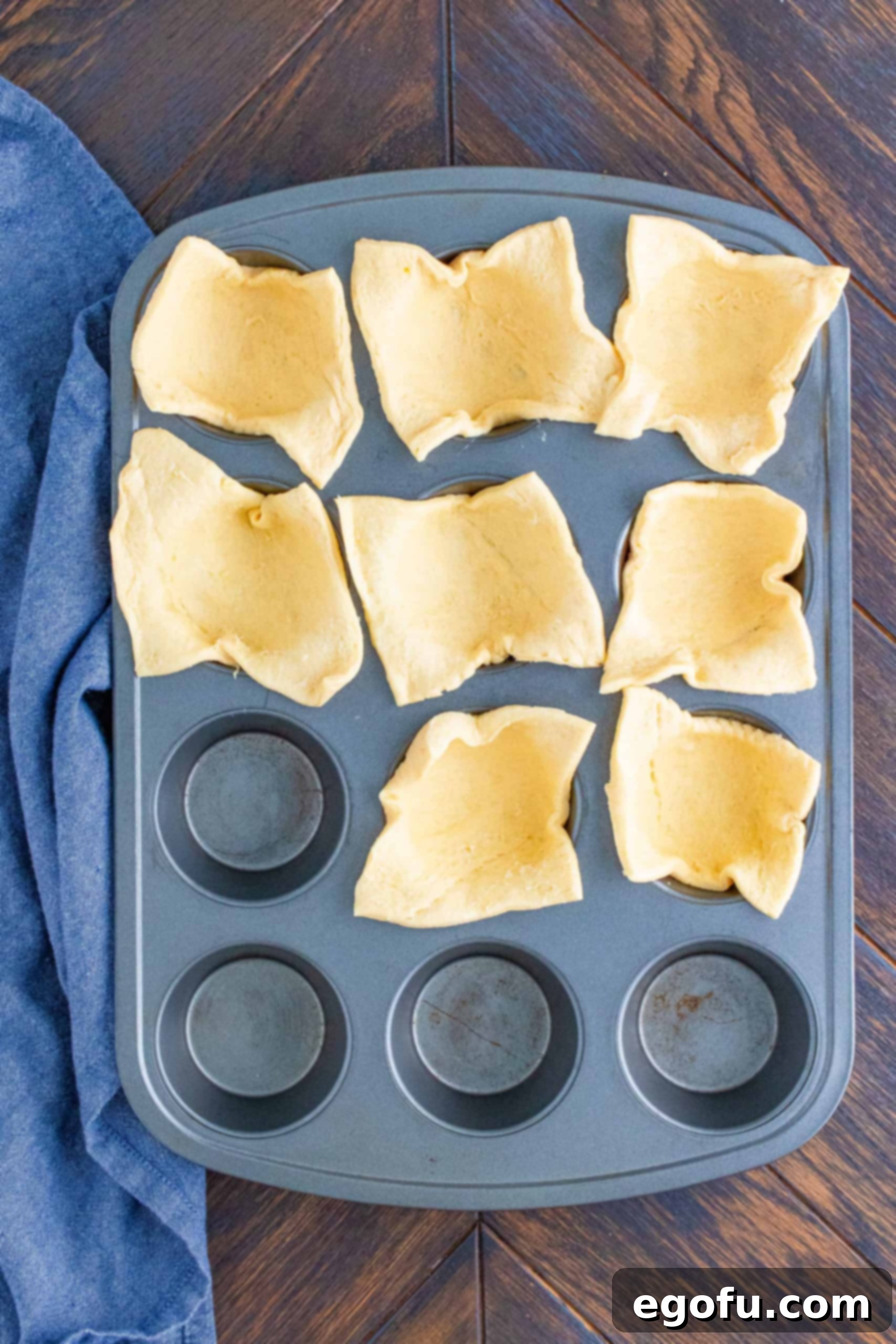 Cut Crescent dough sheets carefully placed into wells of a muffin tin, forming the cup base.