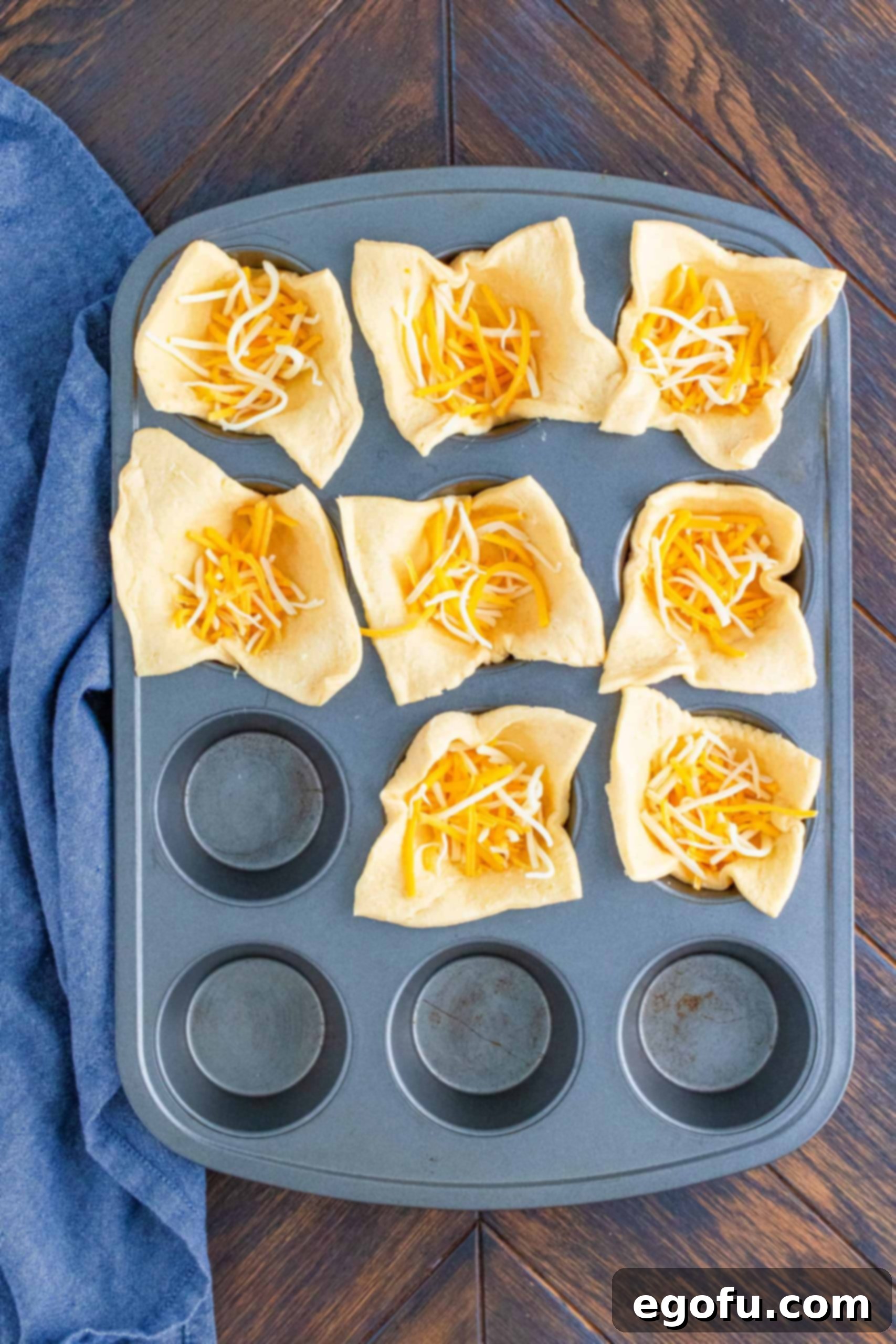 Shredded cheese added to the bottom of crescent dough cups in muffin tin.