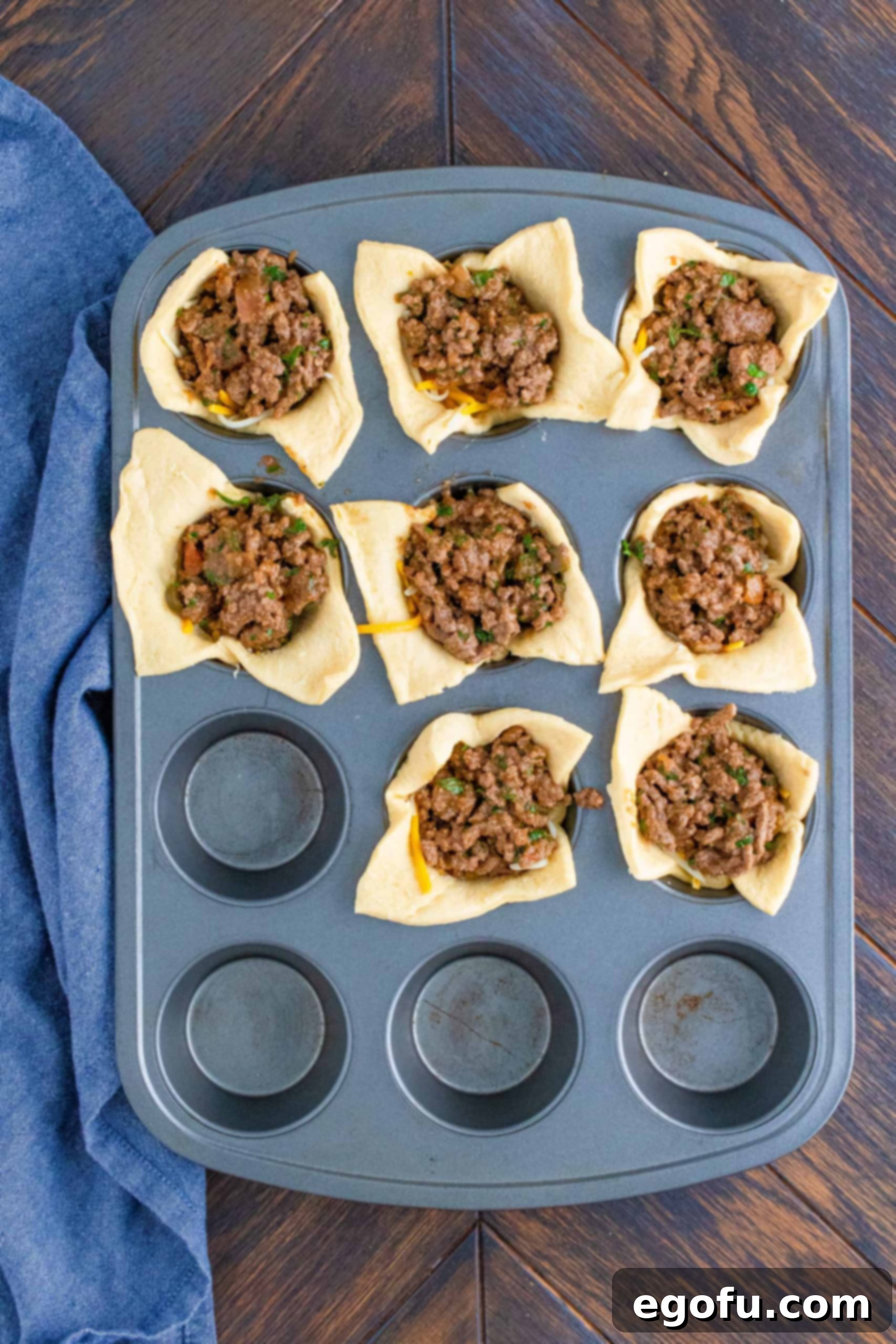 Taco meat filling added over cheese in muffin tin, ready for the next layer.