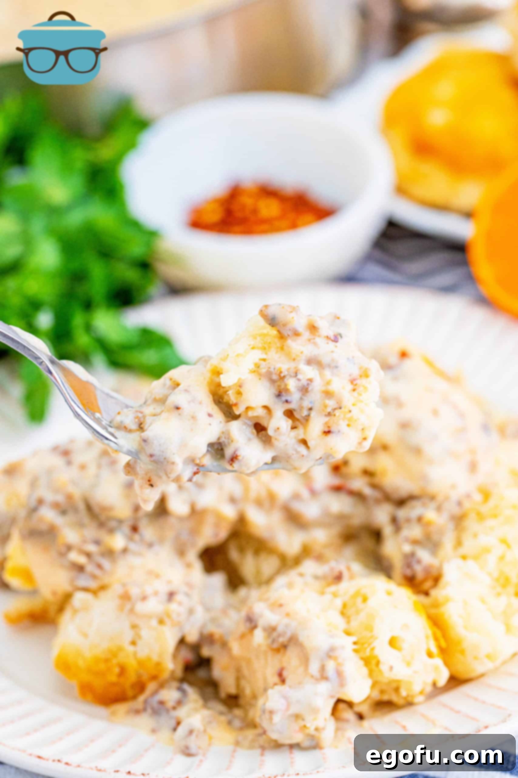 Fork holding up a piece of biscuit topped with Homemade Sausage Gravy, showcasing its creamy texture.