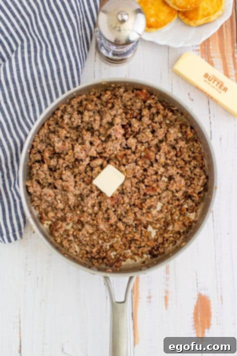 Butter added to cooked sausage in metal pan with striped linen