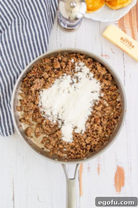 Flour sprinkled over cooked sausage in metal pan with striped linen