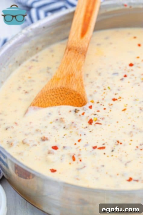 Wooden spoon stirring Homemade Sausage Gravy in metal pan