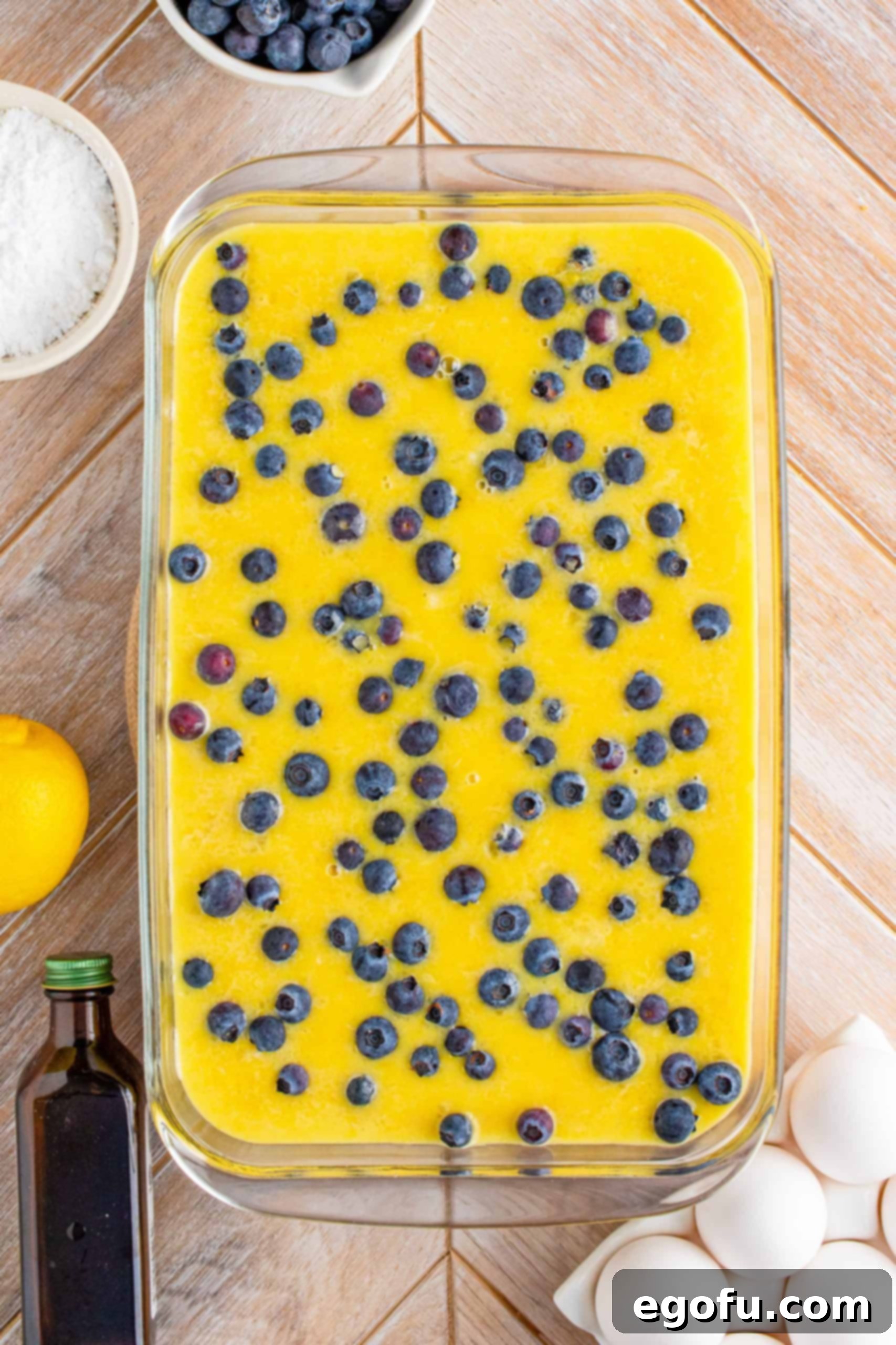Fresh blueberries sprinkled generously over the lemon filling mixture in the baking pan.