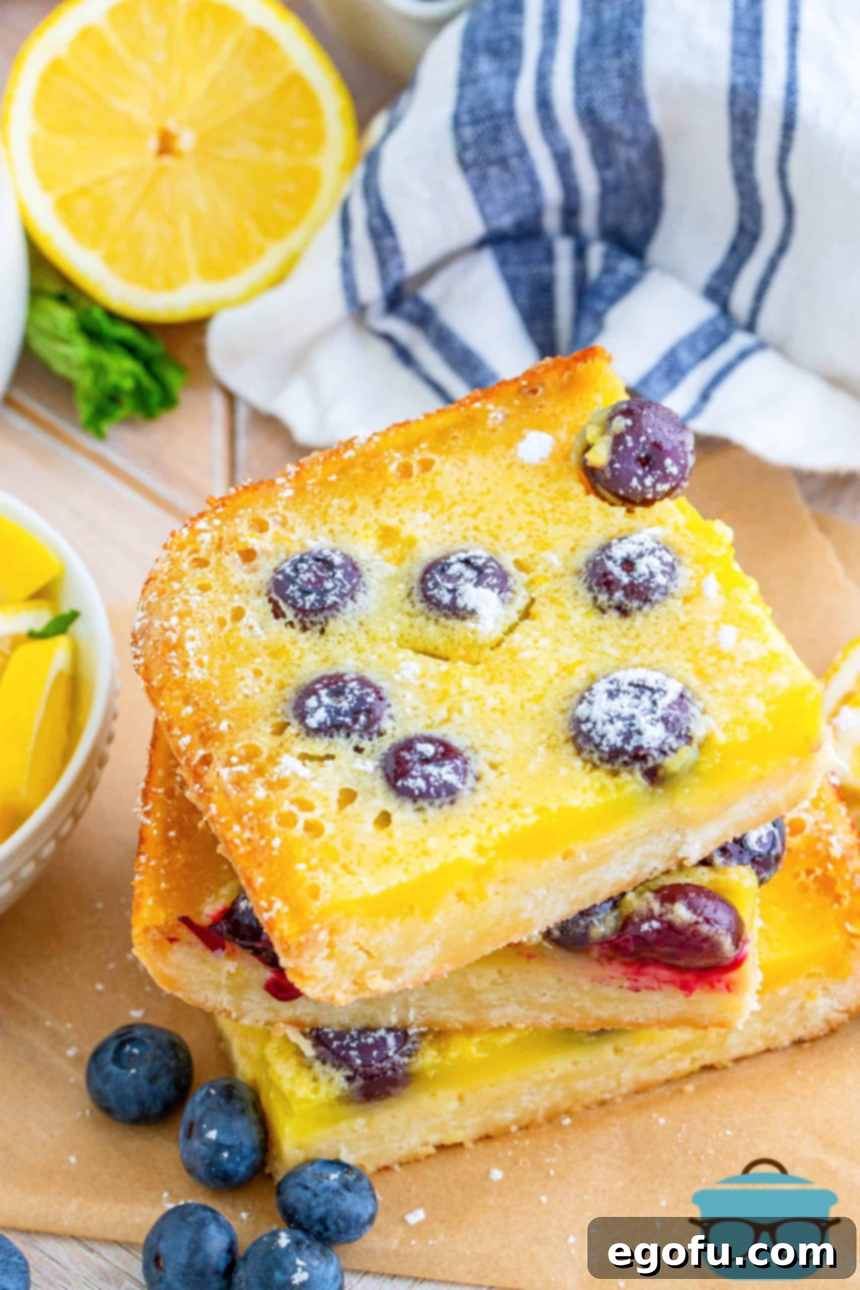 Overhead shot of stacked Blueberry Lemon bars surrounded by loose blueberries on a rustic wooden board, ready for serving.
