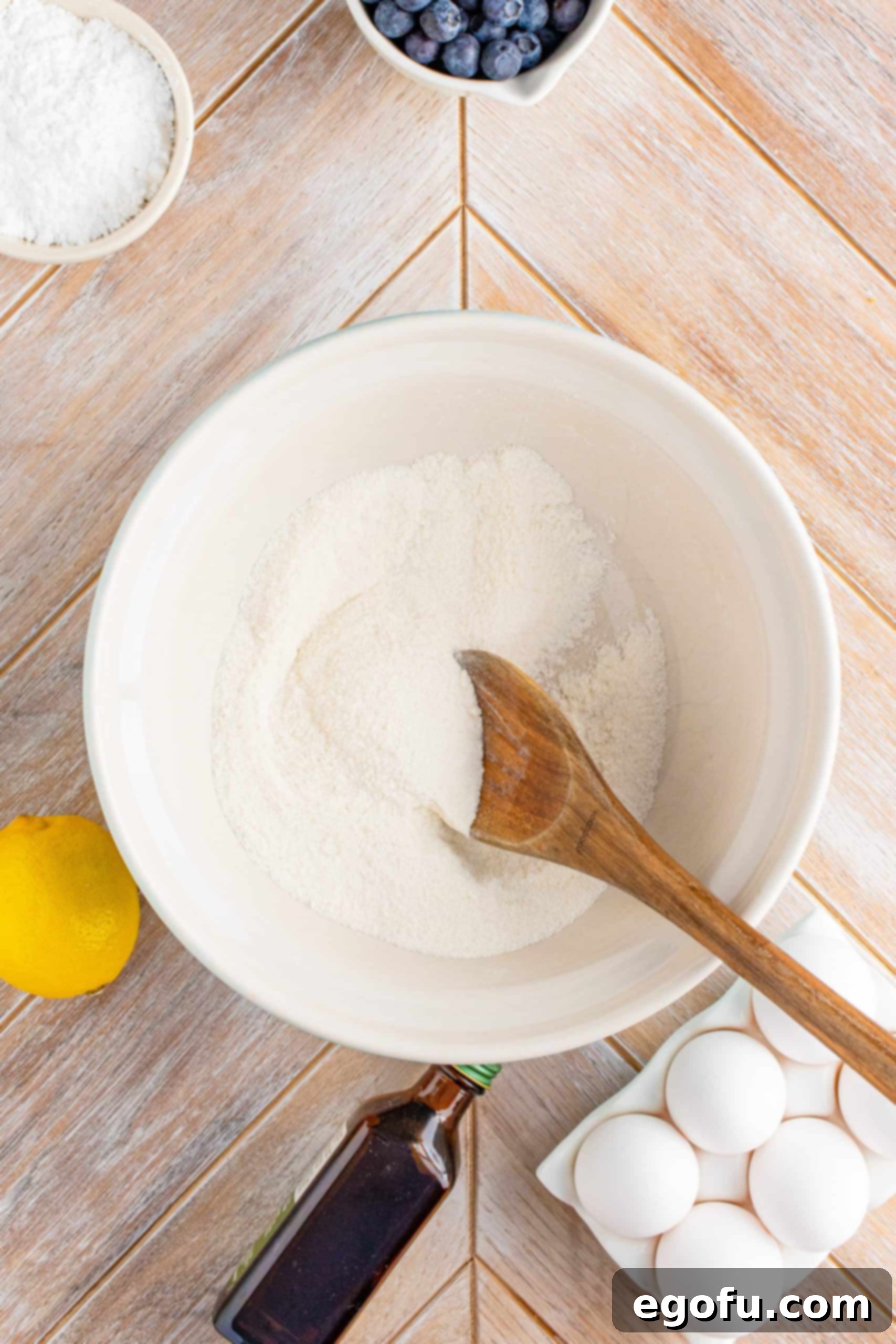 Flour and sugar in a white bowl being stirred with a wooden spoon for the lemon filling.