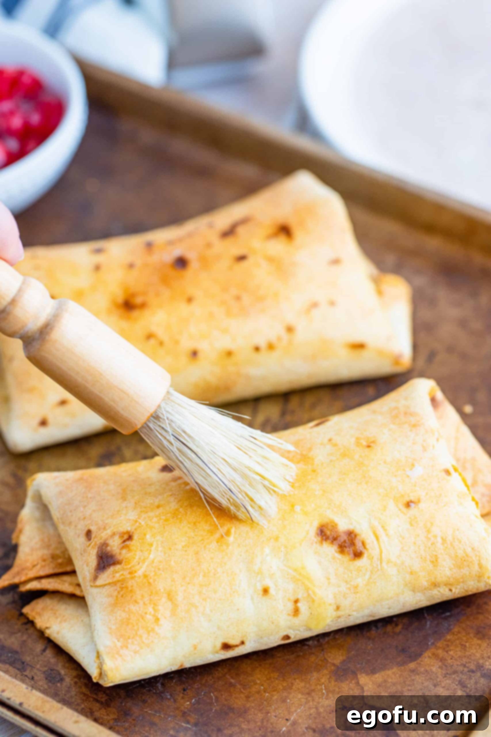Finished Air Fryer Cheesecake Chimichangas being brushed with butter.