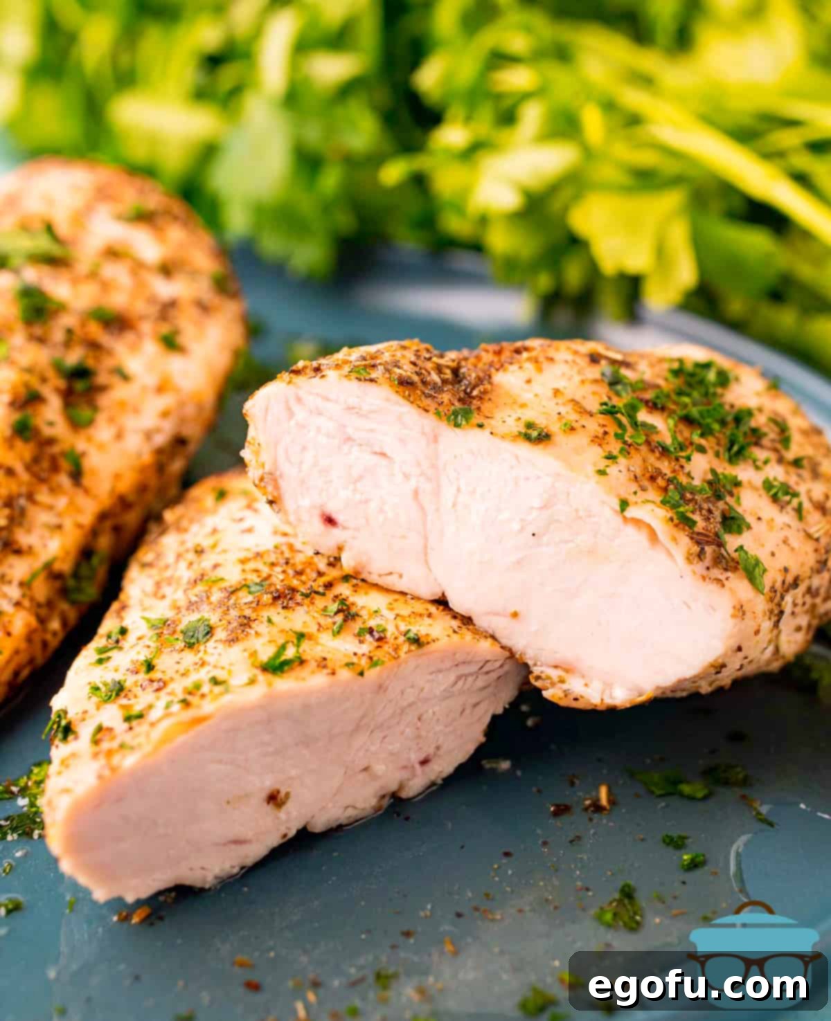 One perfectly cooked air fryer chicken breast sliced in half and stacked on top of another whole breast, resting on a gray plate, revealing its juicy interior.