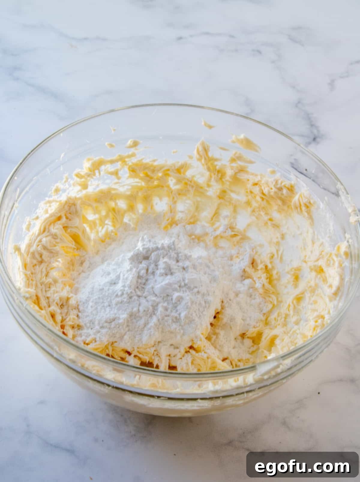 Velvet Banana Delight Cupcakes 14 Powdered sugar being added gradually to the butter mixture in a clear bowl.